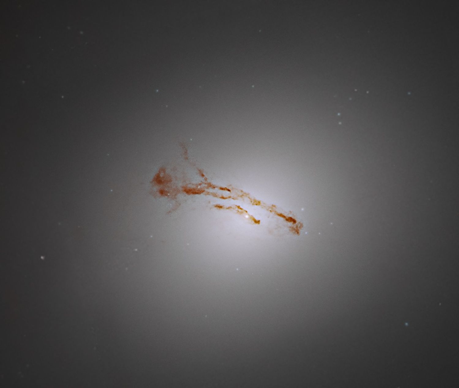 A hazy ball of white light fills the image. The ball is brighter toward the center of the image, becoming more diffuse toward the edges of the image. Bands of rusty-brown dust stretch across the core.