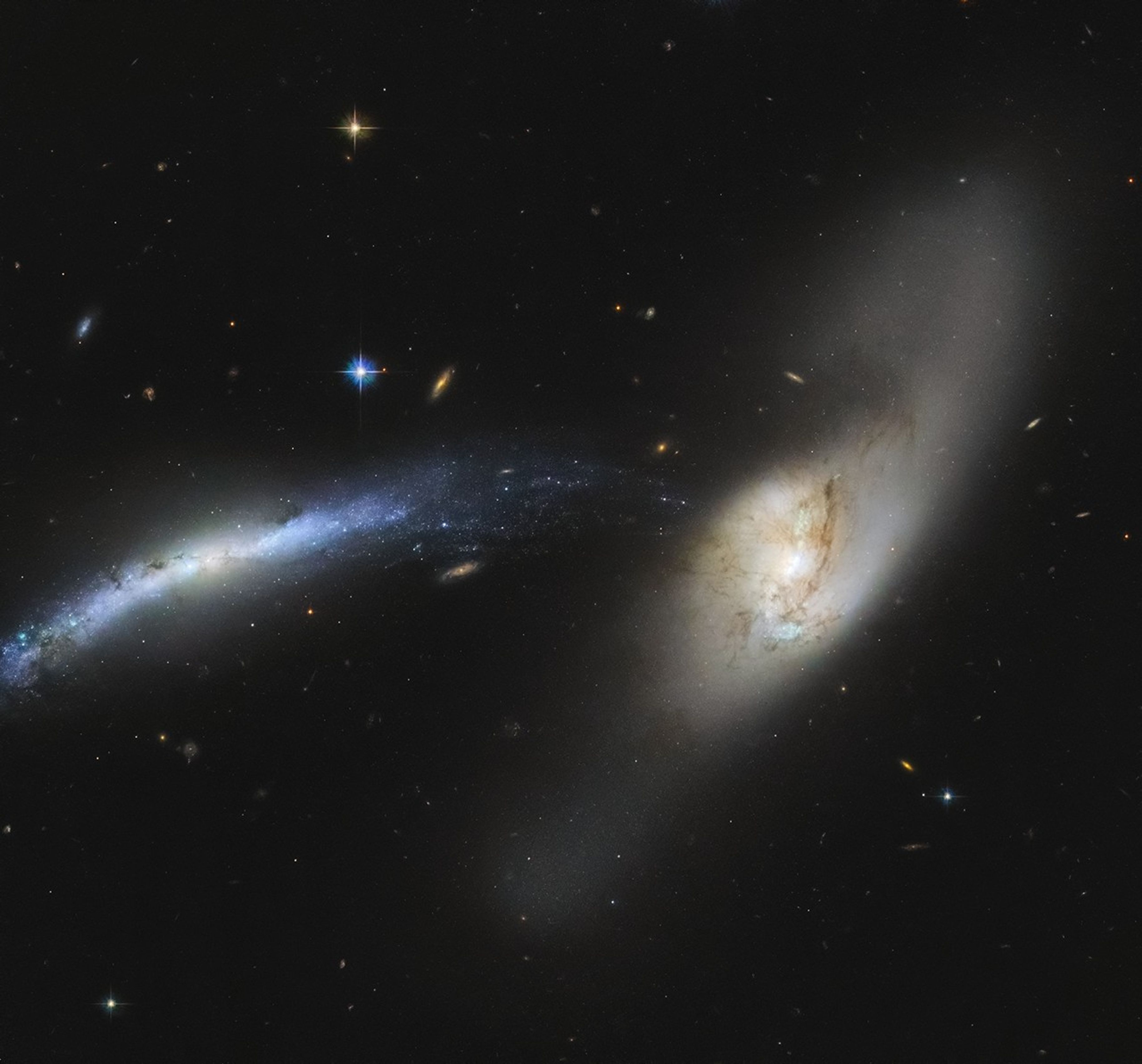 An interacting pair of galaxies. The one at the left of the image likes like a blue-white streak. The one at center-right is whitish with brown streaks. The blue one appears warped, and seems to be getting ripped apart. Rain comes to mind when looking at this, like the stars and gas of the blue galaxy are mere particles condensing and falling into the white galaxy like rain.
