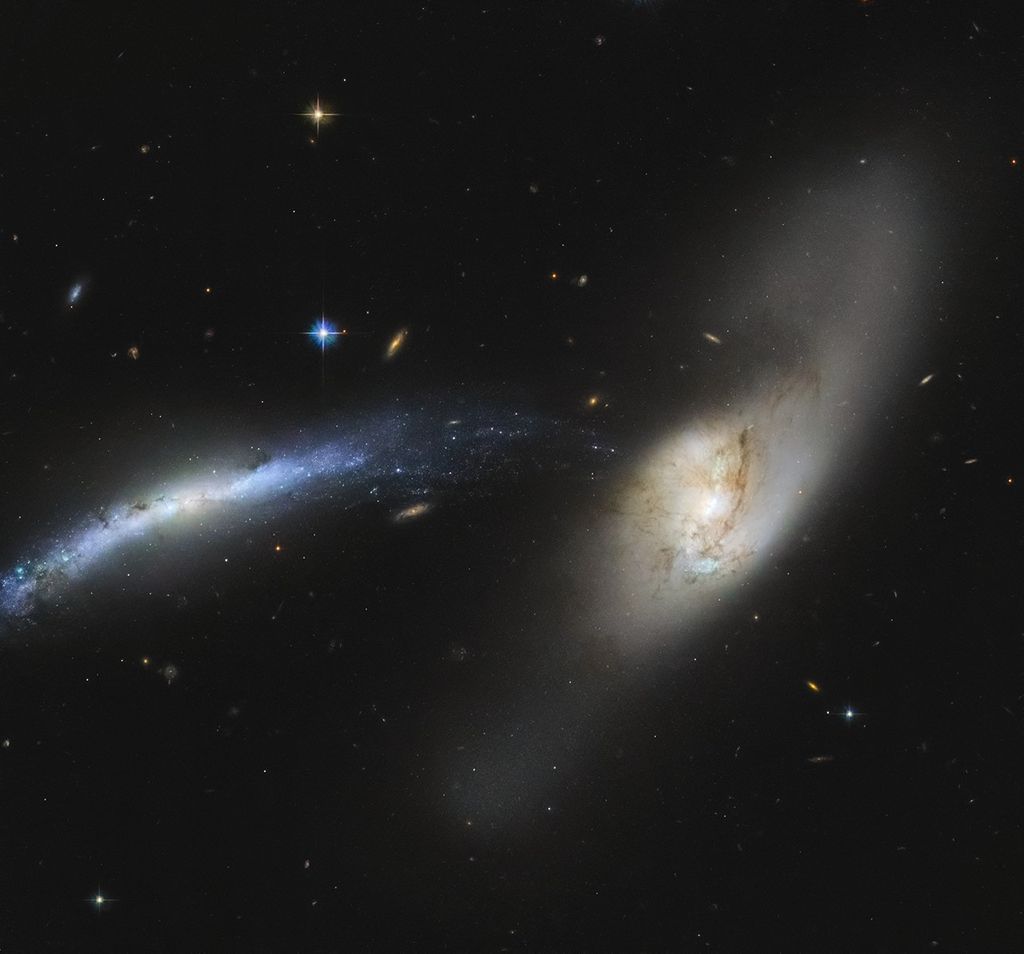 An interacting pair of galaxies. The one at the left of the image likes like a blue-white streak. The one at center-right is whitish with brown streaks. The blue one appears warped, and seems to be getting ripped apart. Rain comes to mind when looking at this, like the stars and gas of the blue galaxy are mere particles condensing and falling into the white galaxy like rain.
