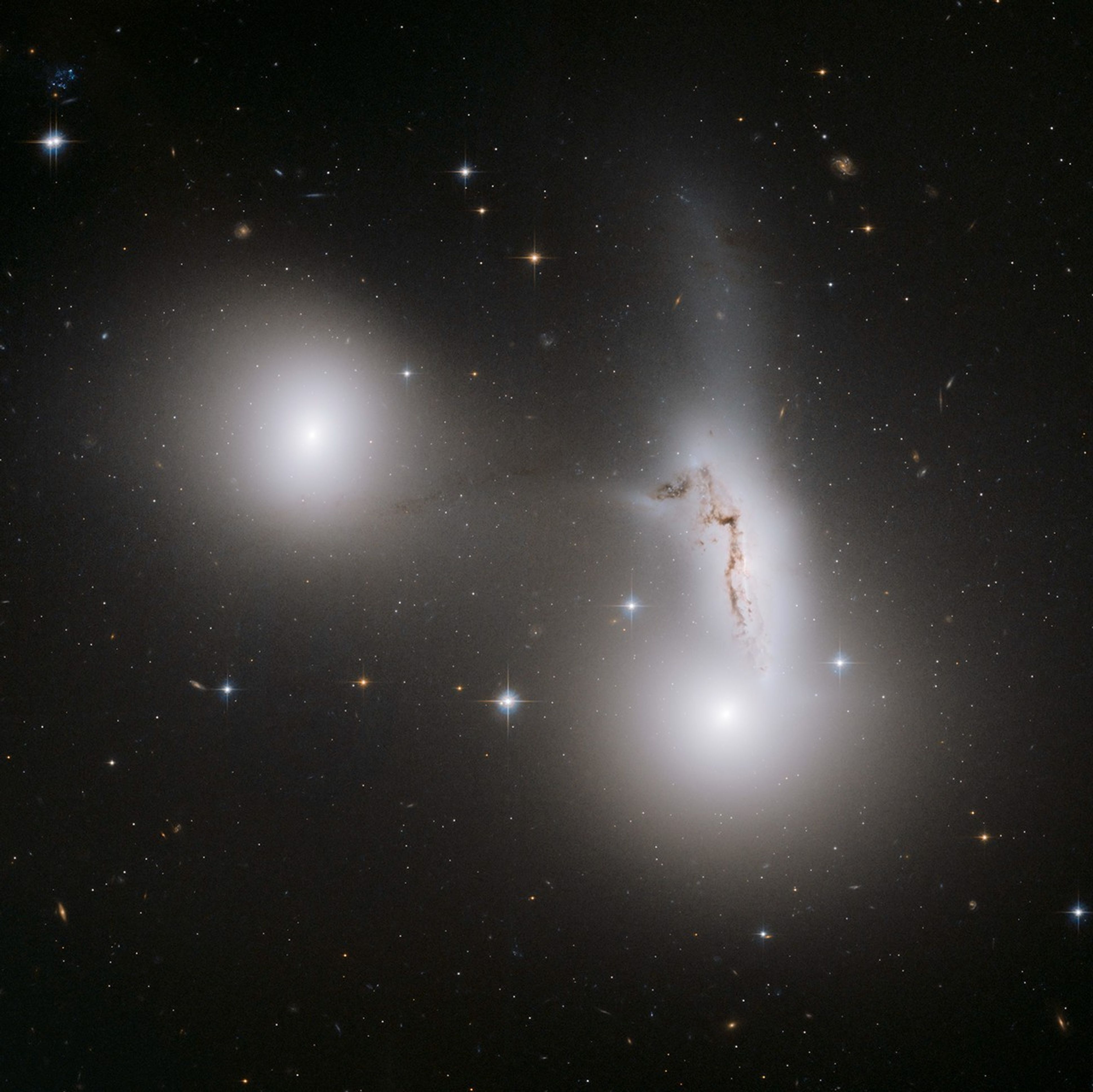 Two glowing white spheres, one on the left above center and one just lower-right of center. Above the right galaxy is a smear of white stars with a streak of brown gas in it.