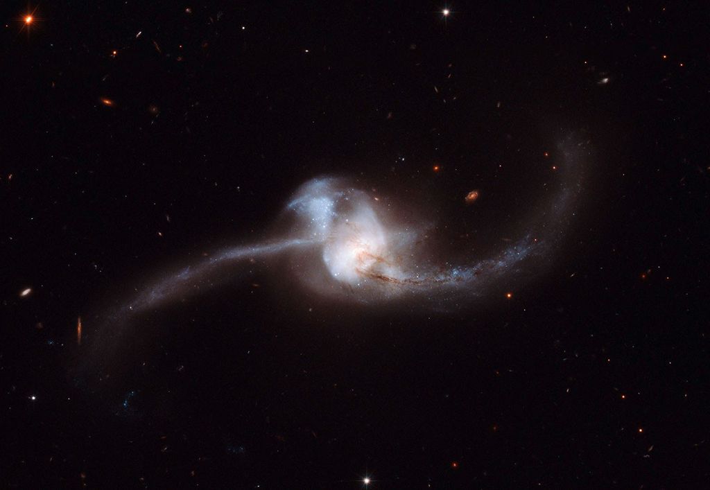 A swirl of white stars in the center with streaks of red-brown dust, with "arms" of stars extending out to the left and right.