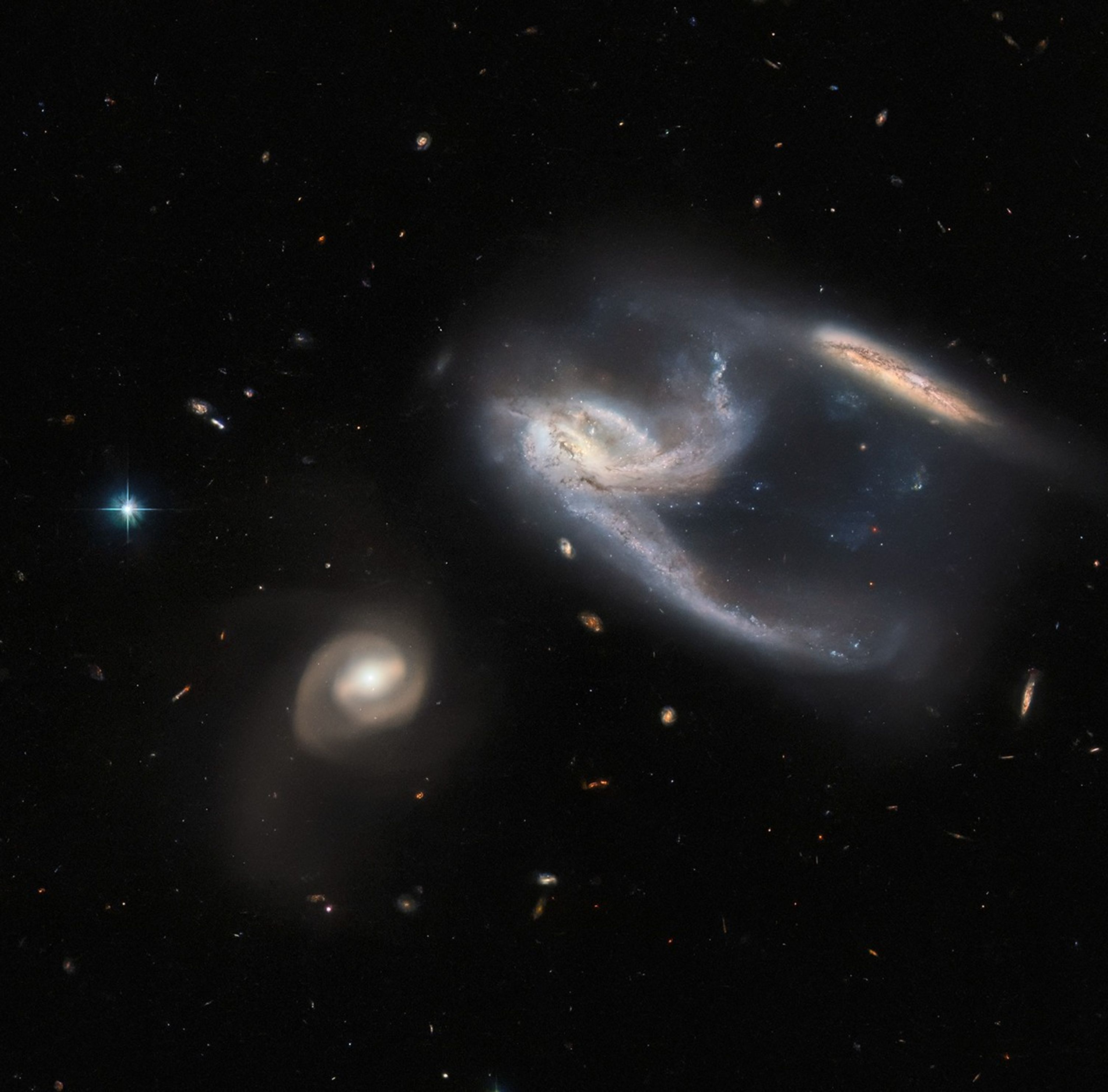 Three galaxies, the center one holds two extended arms, one of which appears to connect to a galaxy at upper right.