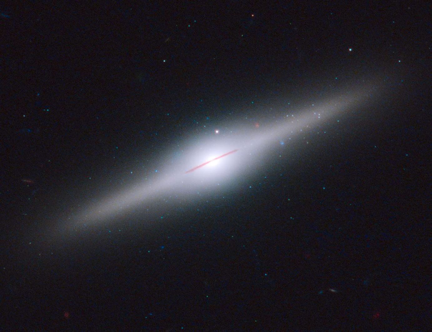 A glowing white halo is shaped like a much larger version of the galaxy inside it, which appears as a flat, edge-on red-brown disk with a glowing white center. Dozens more stars and galaxies in the background.