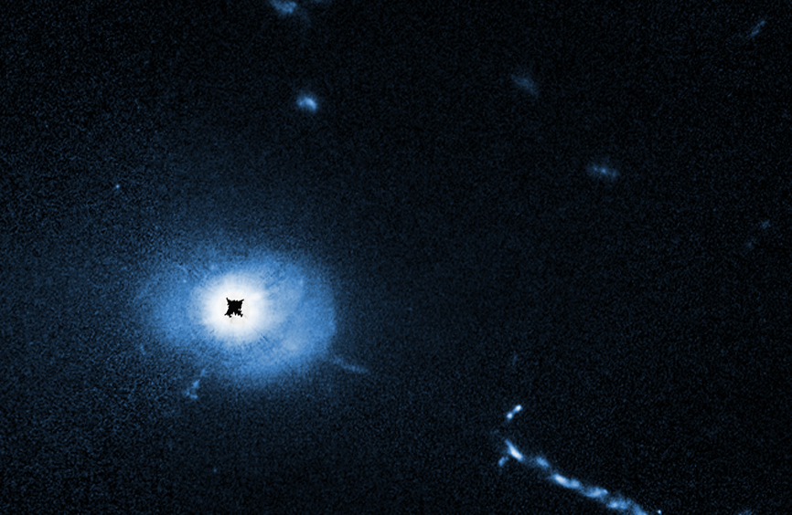 A two-panel annotated image of quasar 3C 273, taken by different Hubble science instruments. The top panel is a Hubble Wide Field Planetary Camera 2 (WFPC2) image of quasar 3C 273. It looks like a bright white car headlight. There is a linear orange-white smoke-like feature stretching to the 4 o’clock position, an extragalactic jet launched from the quasar in the center of the black hole of an unseen galaxy. The bottom panel is a Hubble Space Telescope Imaging Spectrograph (STIS) coronagraph image of quasar 3C 273. It looks the same as the WFPC2 image, but in shades of blue. A black circle (labeled “core light blocked”) blocks the glare of the quasar. Blue-colored filamentary material is visible near the black hole. The extragalactic jet is still visible.