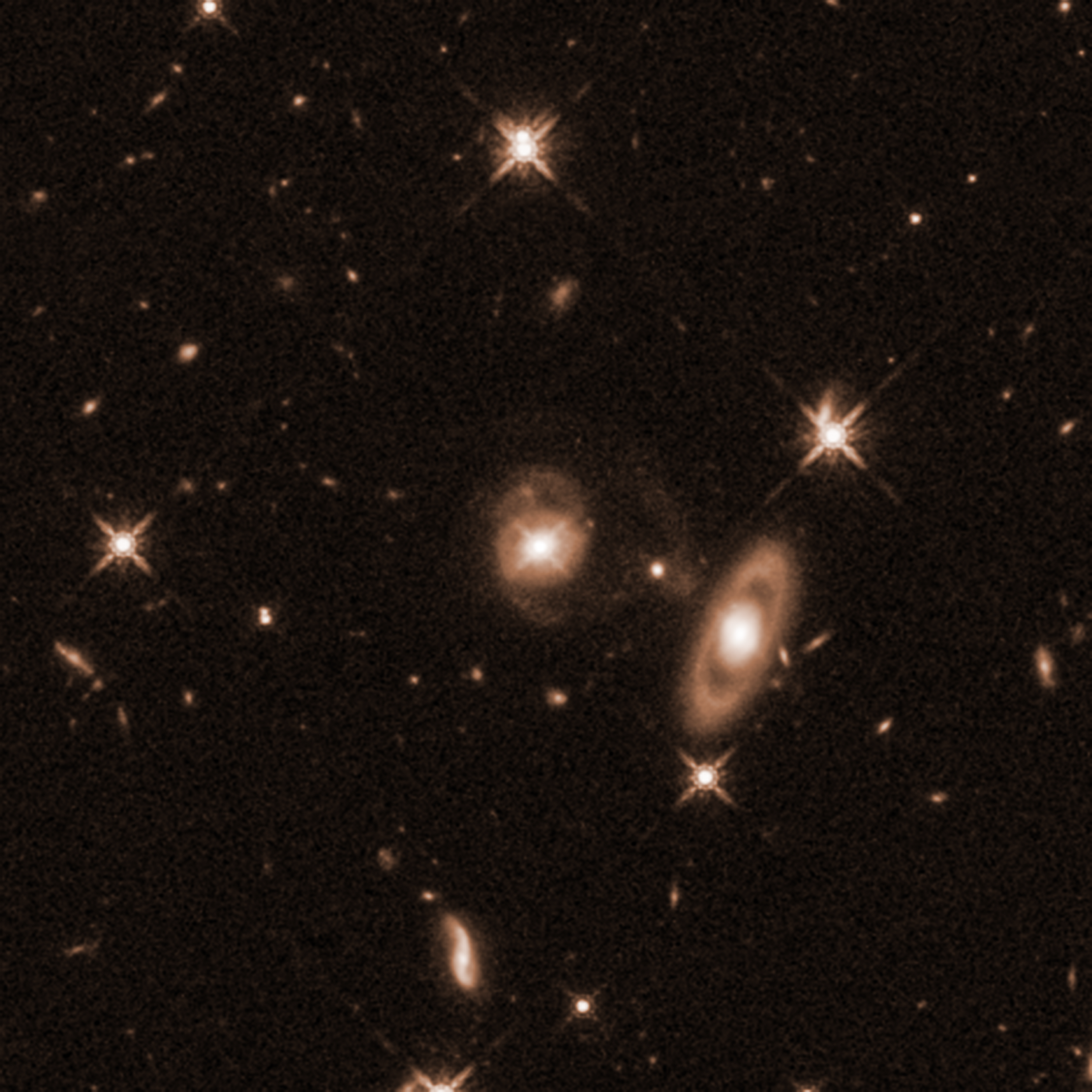 Field of yellow galaxies of various sizes and distances on a black background. Two larger galaxies are prominent. Centered is a galaxy with a bright core and faint spiral arms coming off its top and bottom. To the lower right of the spiral is a ring galaxy with an apparent gap between its bright core and the ring oval of dust and gas surrounding it.