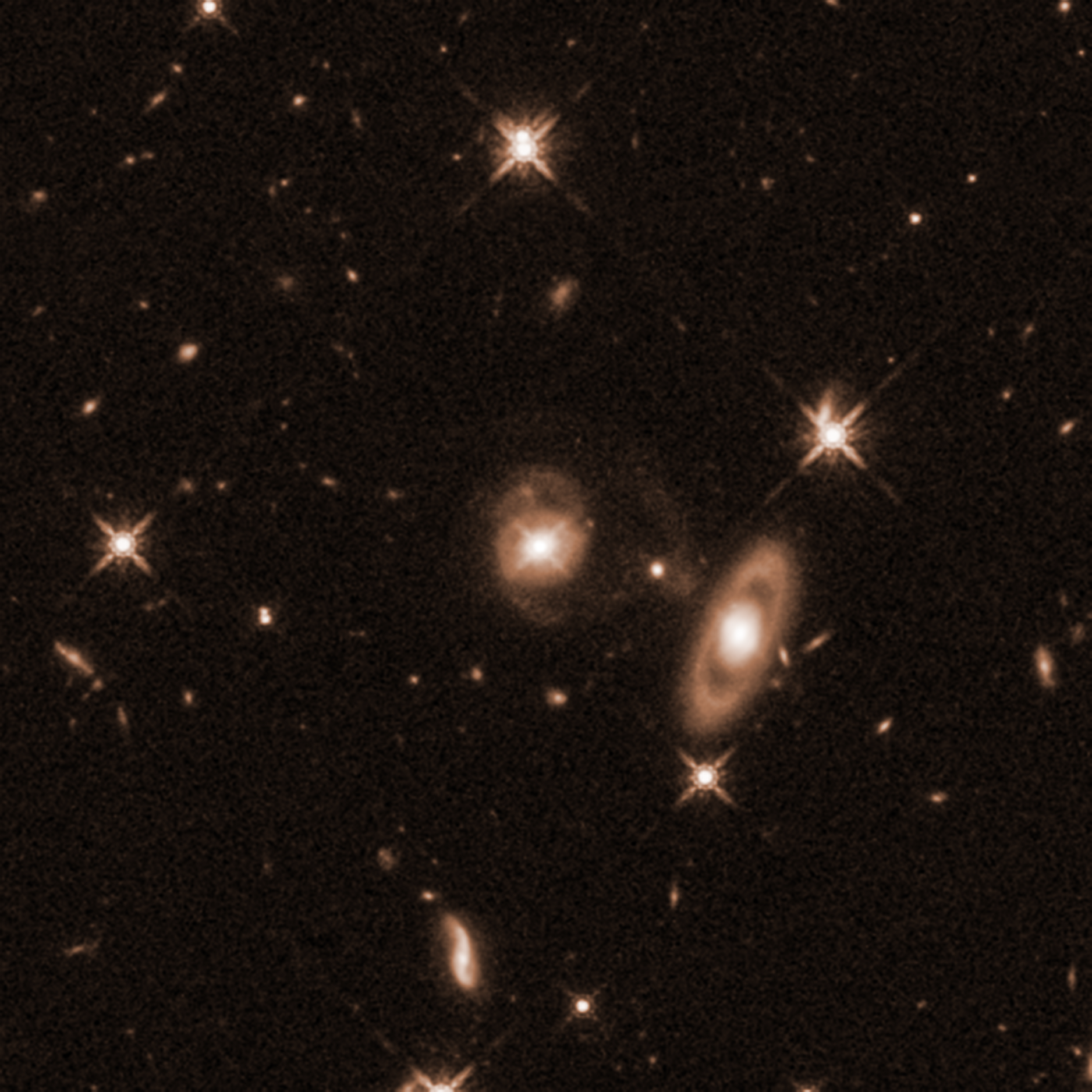 Field of yellow galaxies of various sizes and distances on a black background. Two larger galaxies are prominent. Centered is a galaxy with a bright core and faint spiral arms coming off its top and bottom. To the lower right of the spiral is a ring galaxy with an apparent gap between its bright core and the ring oval of dust and gas surrounding it.