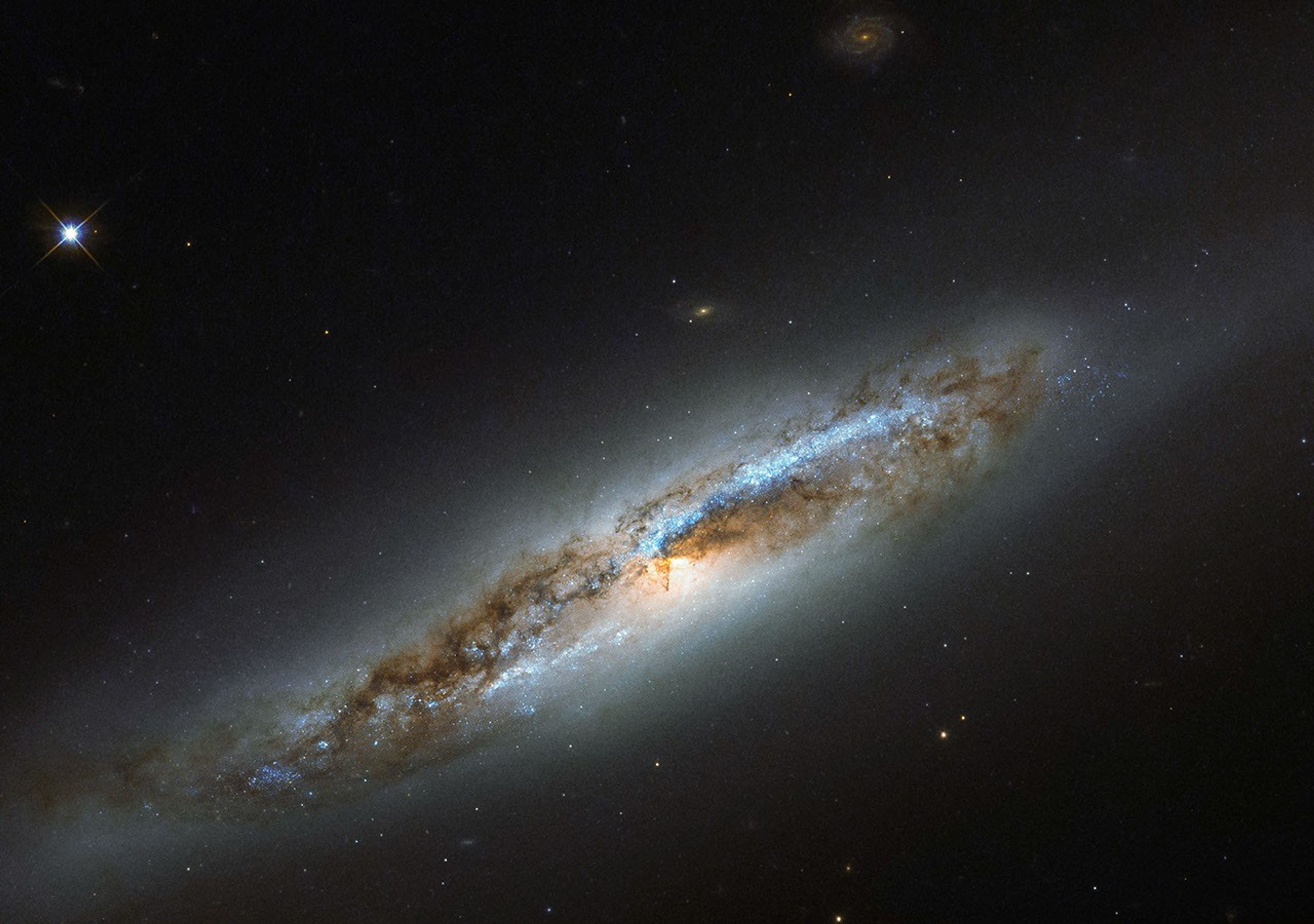 A nearly edge-on spiral galaxy. Its disk holds blue light from clusters of hot stars. Thick dark clouds of dust block the strong white light from galaxy’s center. A faint, glowing halo of gas surrounds the disk, fading into the black background of space.