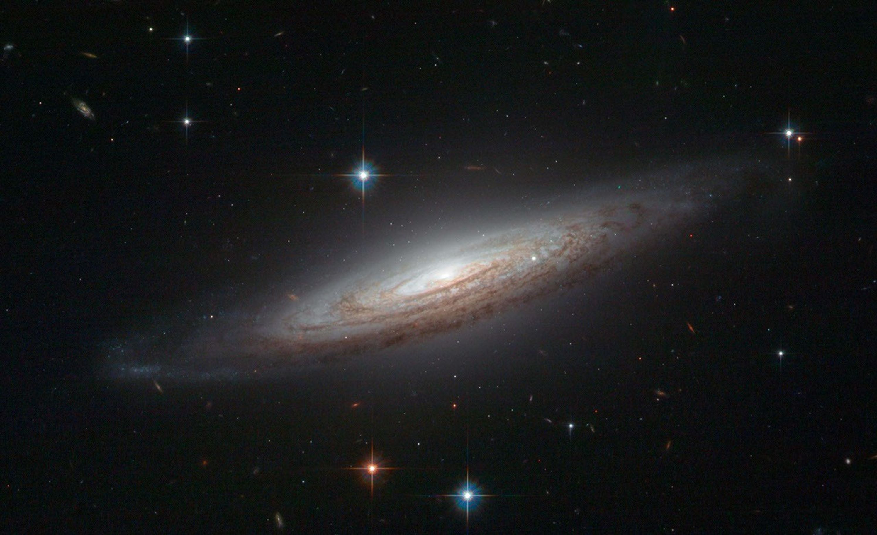 Wispy dark spirals outline the white center of a galaxy, with hundreds more stars and galaxies dotting the black background.