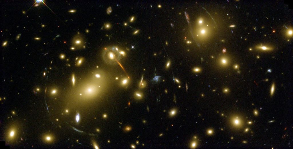 Bright yellow-white galaxies fill the field of view. Faint streaks and arcs of gravitationally lensed background galaxies.