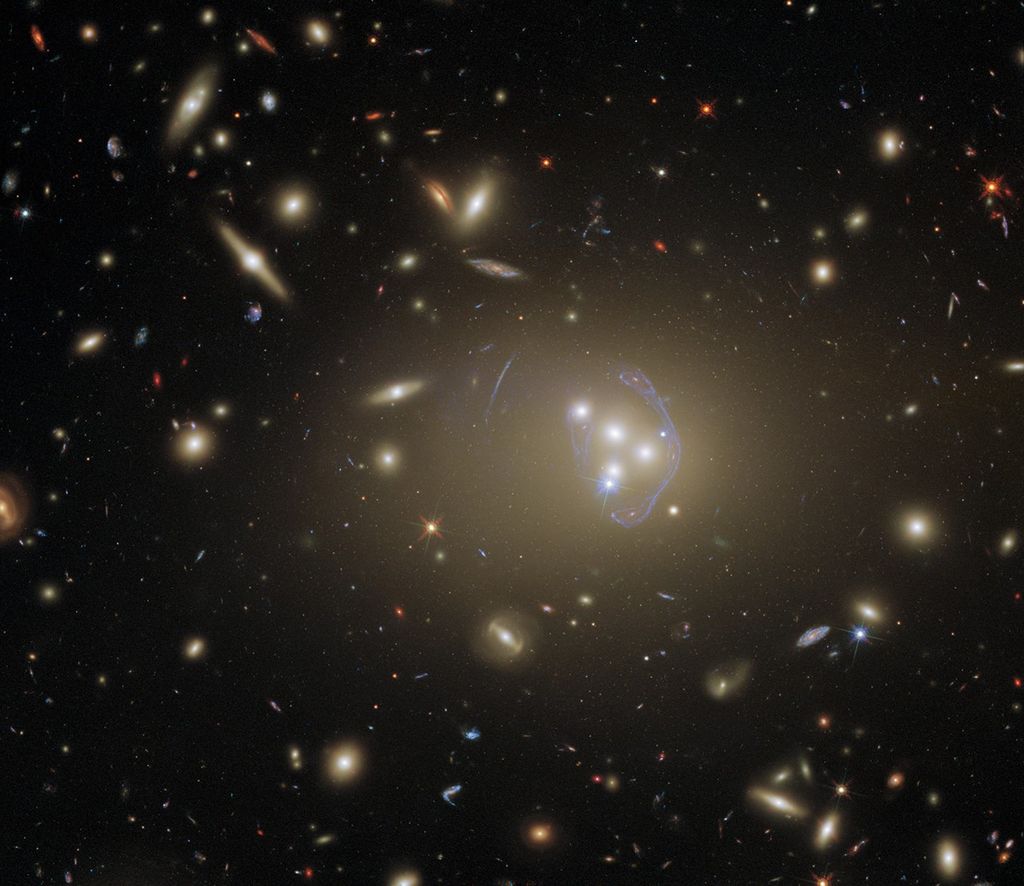 A black background dotted with galaxies. Image center holds a trio of galaxies forming a triangle, with a fourth to the left, and a distinct arc nearly surrounding it.