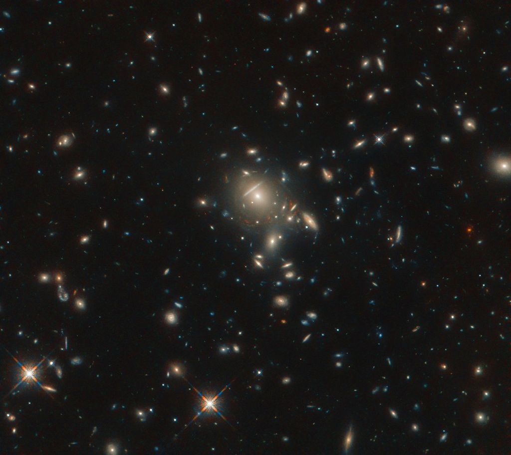Starburst galaxy plck g045.1+61.1: a bunch of bright smears of light against the black backdrop of space, with a clump near the center that have the circular lensing effect.