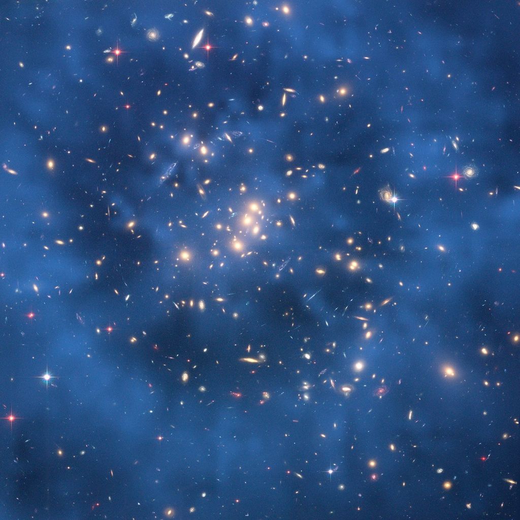 A massive galaxy cluster full of galaxies of all shapes and sizes, which seem to be surrounded by a bluish haze throughout the image.