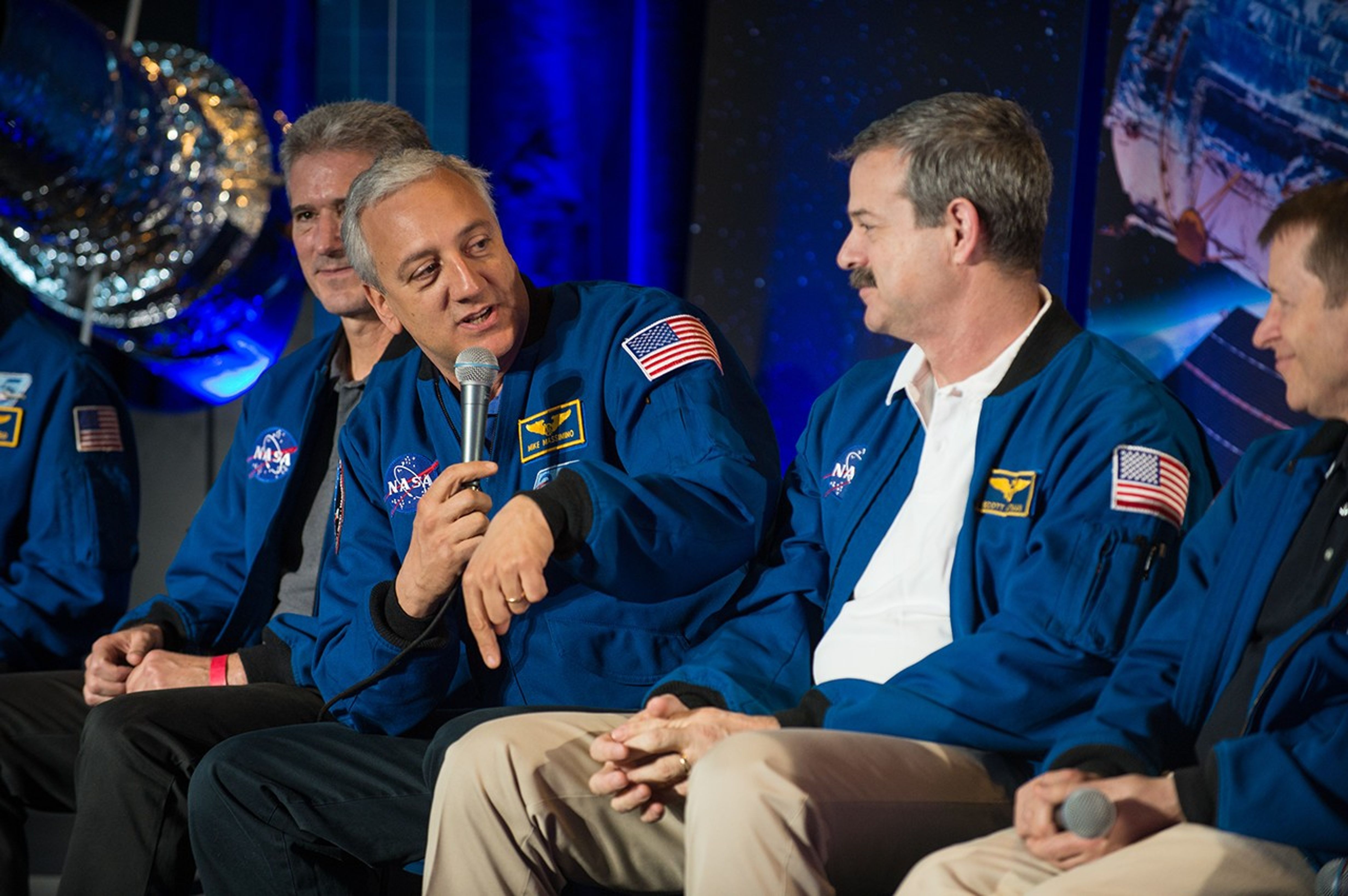 Astronaut Mike Massimino speaks on the panel while looking toward the right side of the photo, towards astronauts seated to his left.