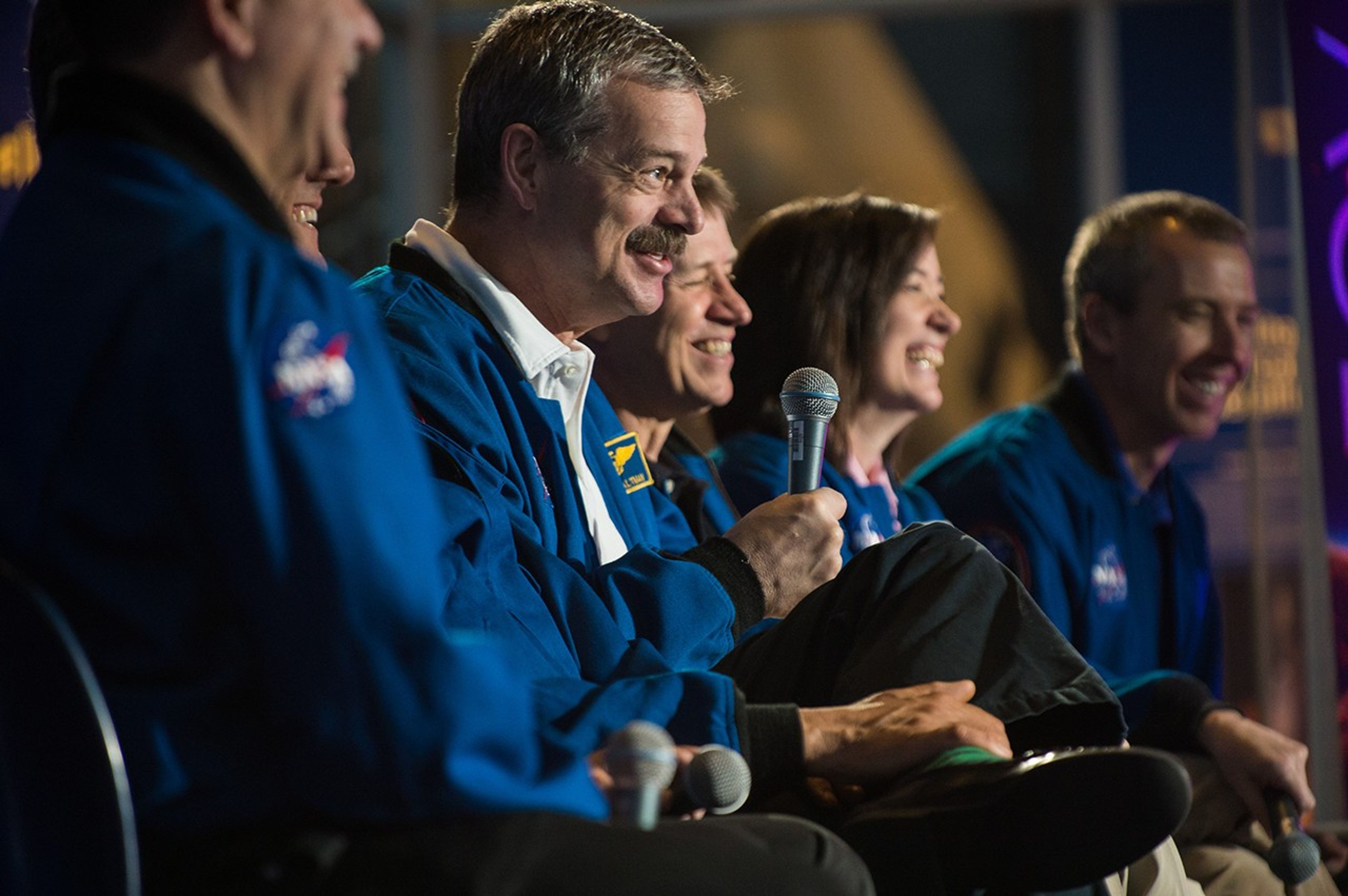 Scott Altman, sitting in the center of the panel, addresses the crowd while his fellow astronauts smile and laugh from his words.