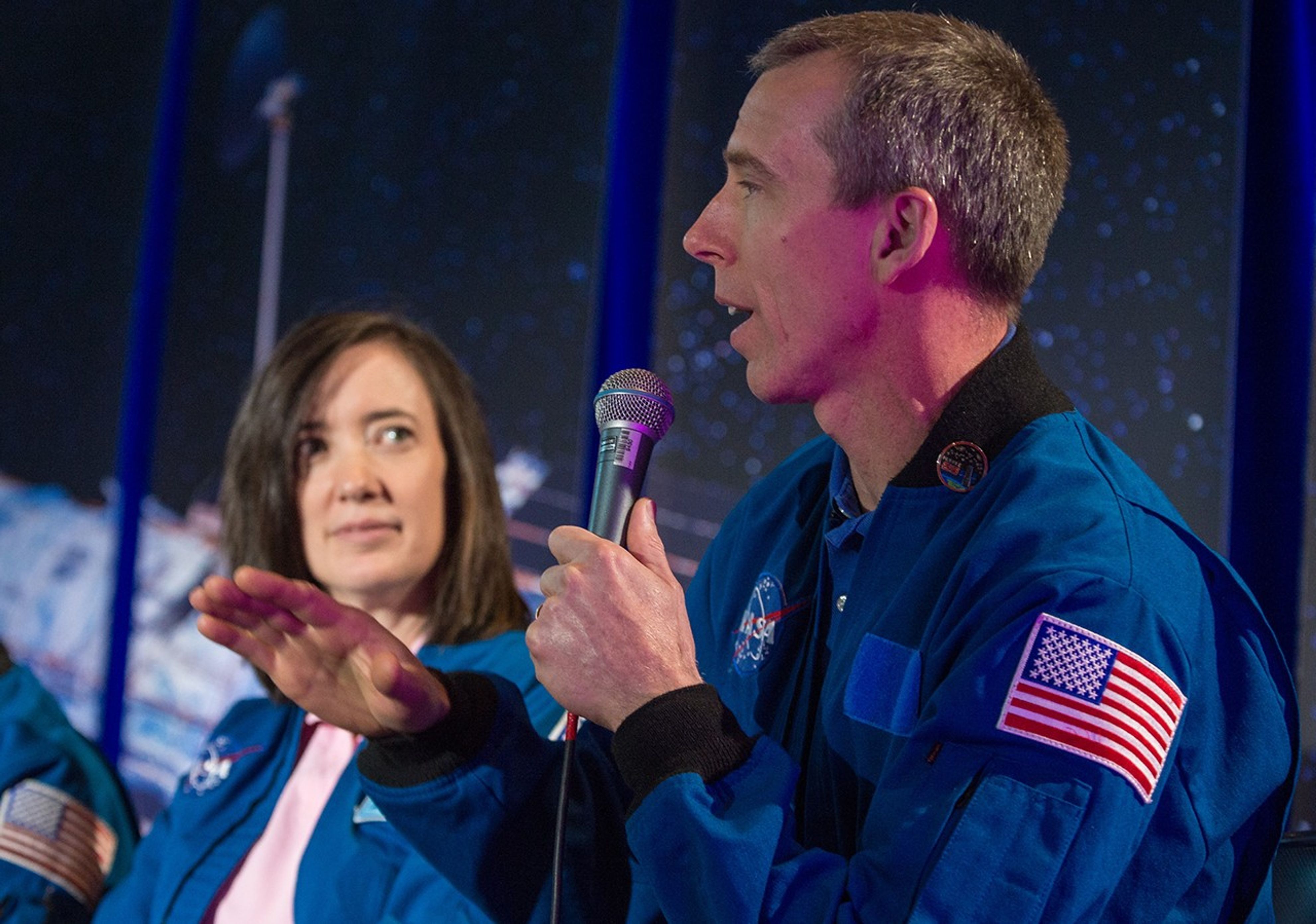Drew Feustel, right, address the audience. In the background, fellow astronaut Megan McArthur Behnken, left, faces him.