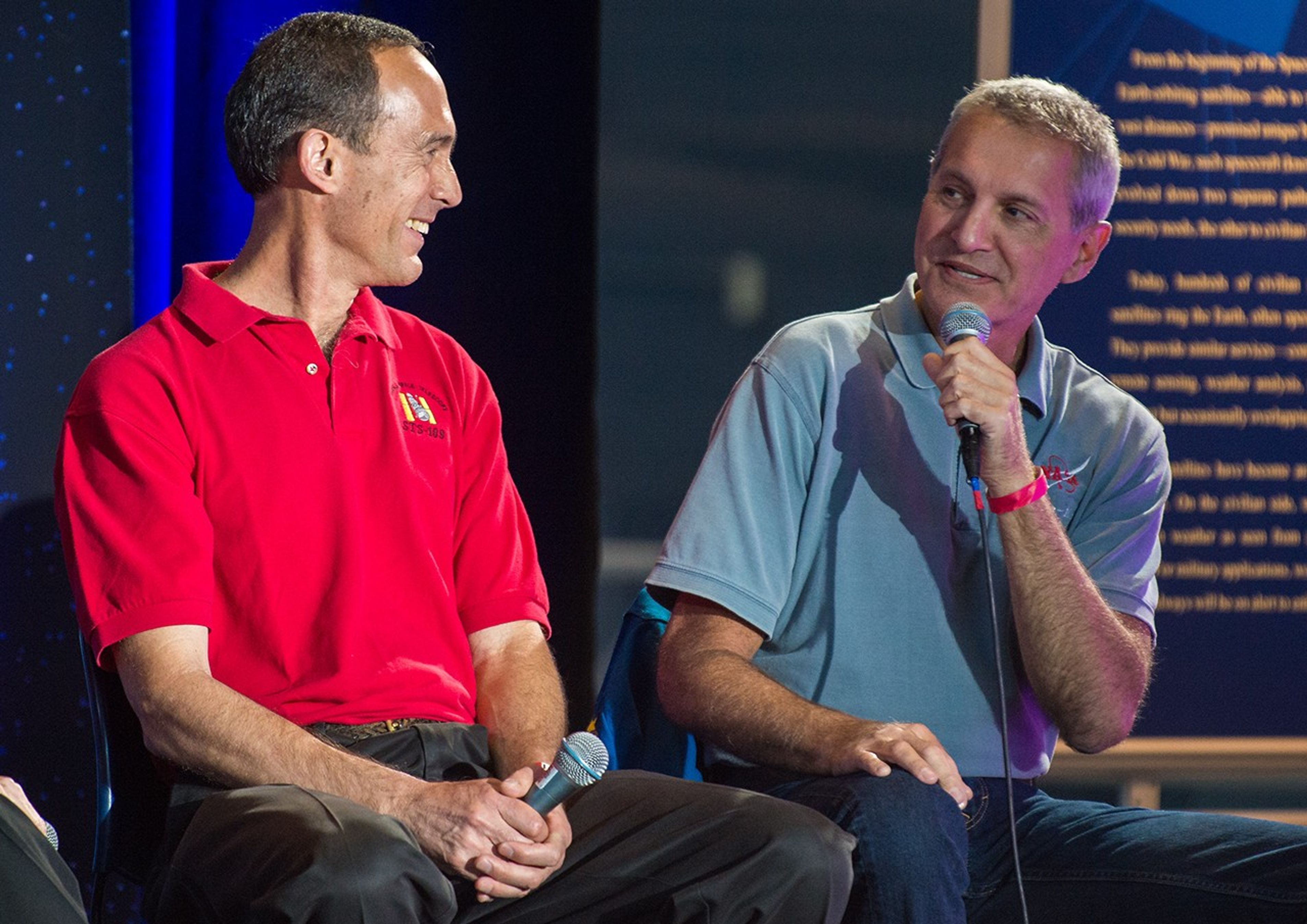 Richard Linnehan, right, speaks to the audience while facing his fellow panelists, while Jim Newman, left, smiles at his words.