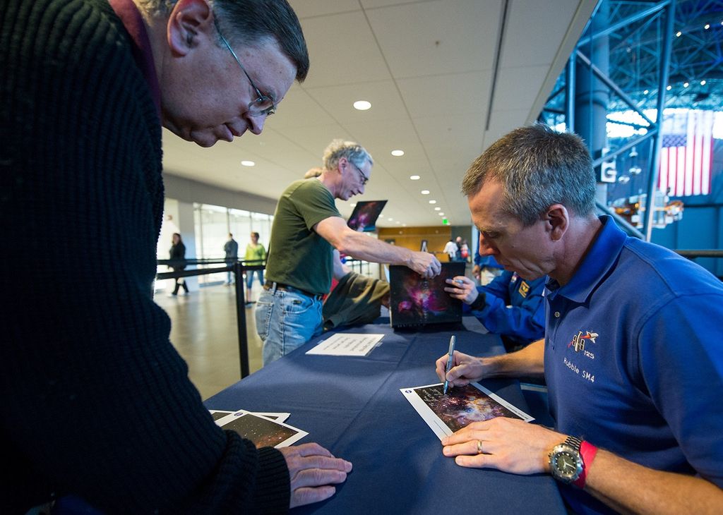 Drew Feustel, right, signs a picture of Westerlund for a museum visitor, left.