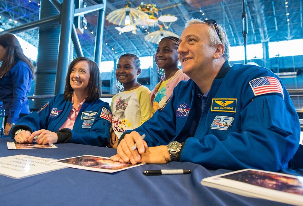 Astronauts McArthur Behnken, left, and Massimino, right, pose for a photo with two young girls, center.
