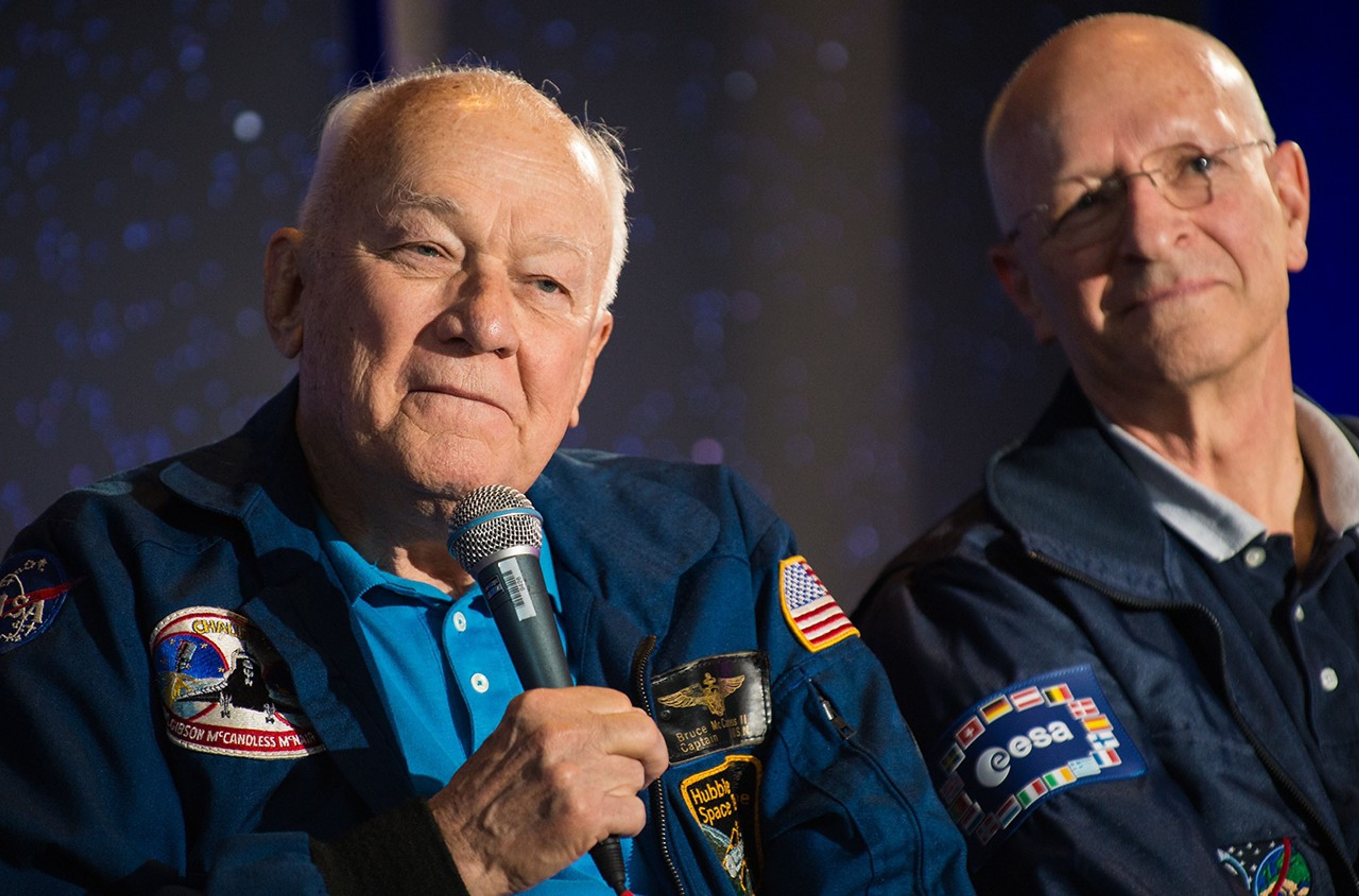Astronaut Bruce McCandless, left, addresses the audience next to fellow panelist and ESA astronaut Claude Nicolllier, right.