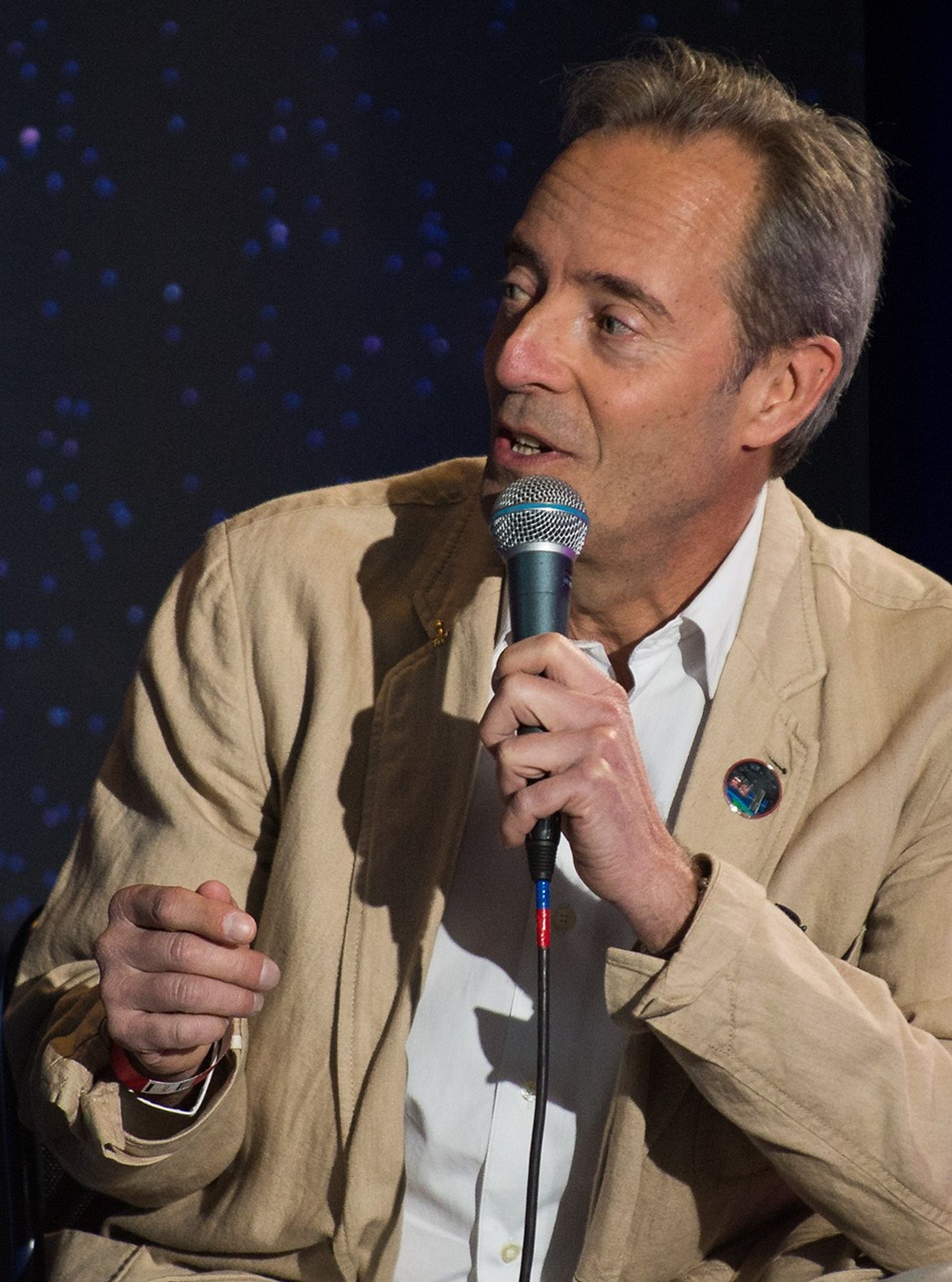 Astronaut Jean-Francois Clervoy holds a mic and addresses the audience.