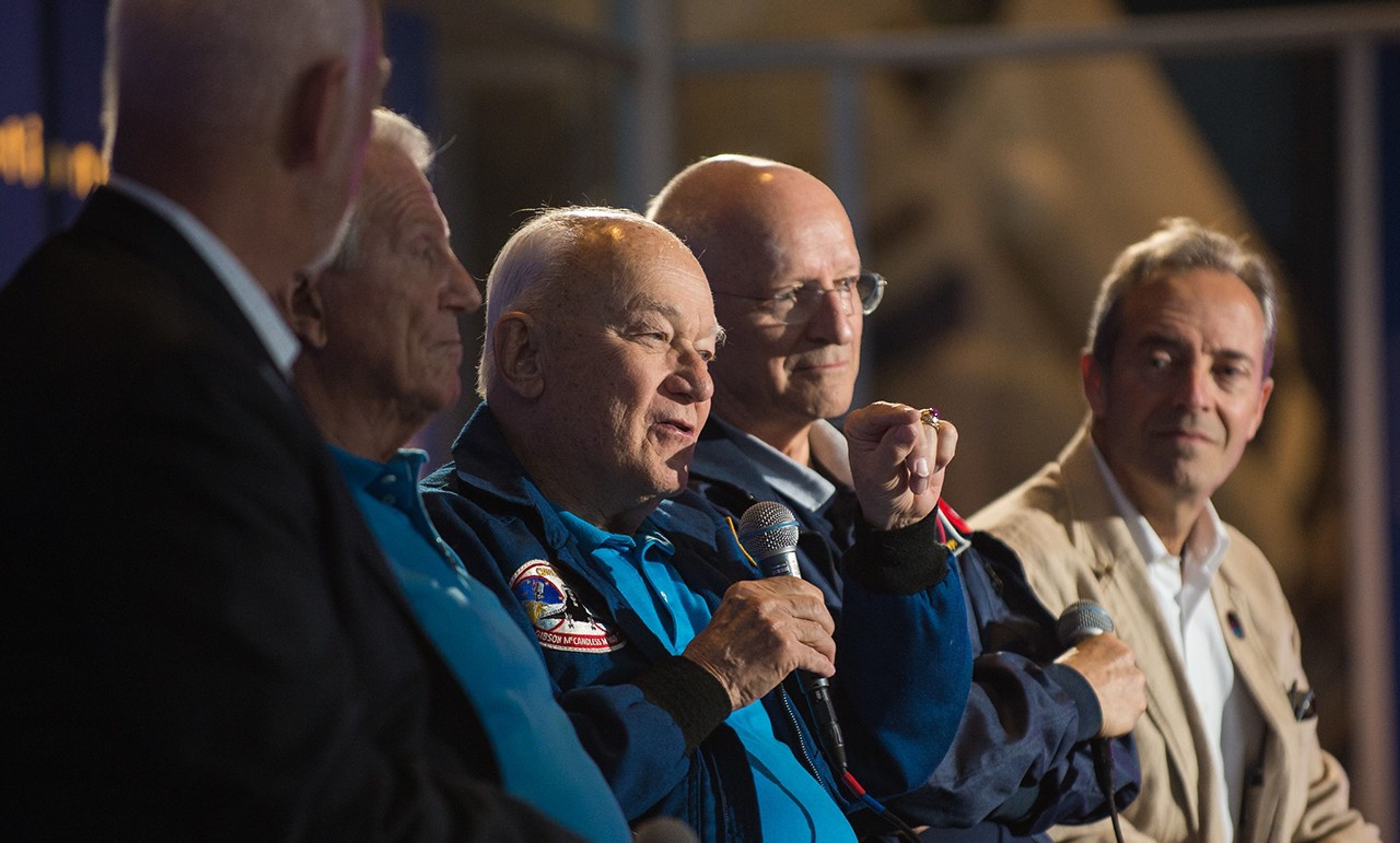 Bruce McCandless, center, addresses the audience while sitting on the panel with four fellow astronauts.