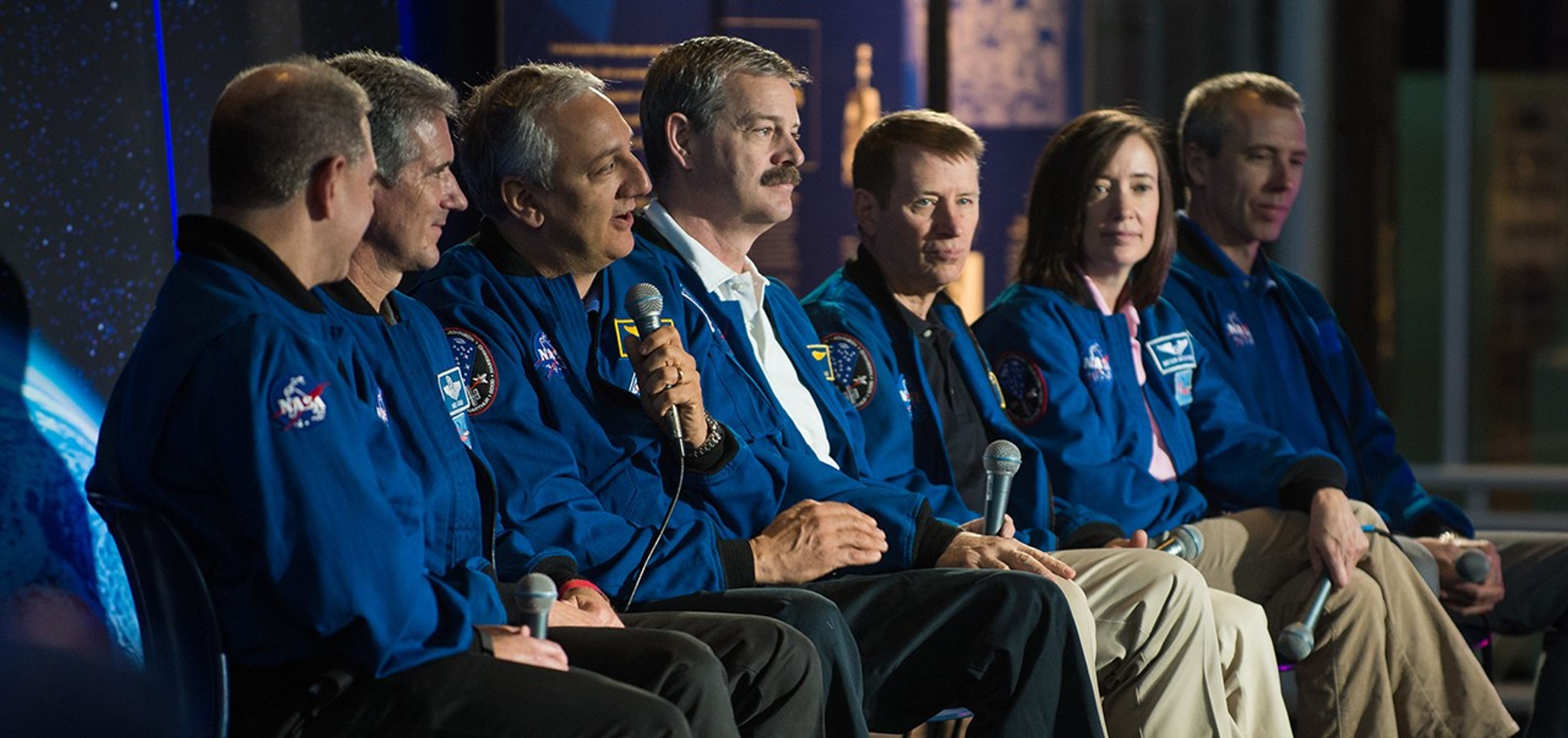 Astronaut Mike Massimino, third from the left, speaks to the audience while the other six astronauts listen.