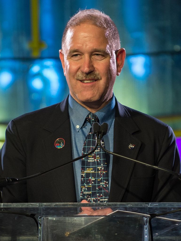 John Grunsfeld stands at the podium, addressing the audience.