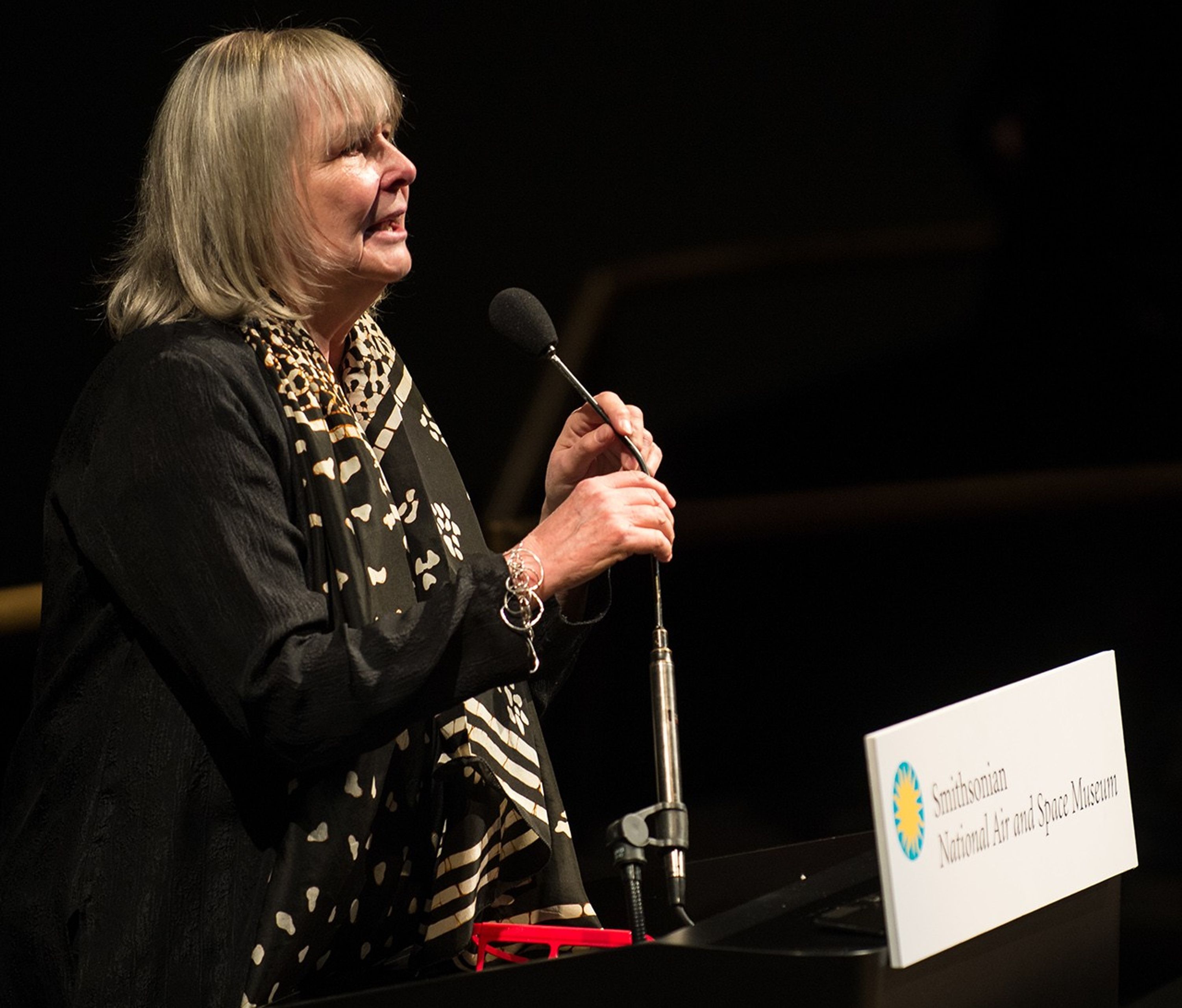 Toni Myers stands at the podium, addressing the audience.