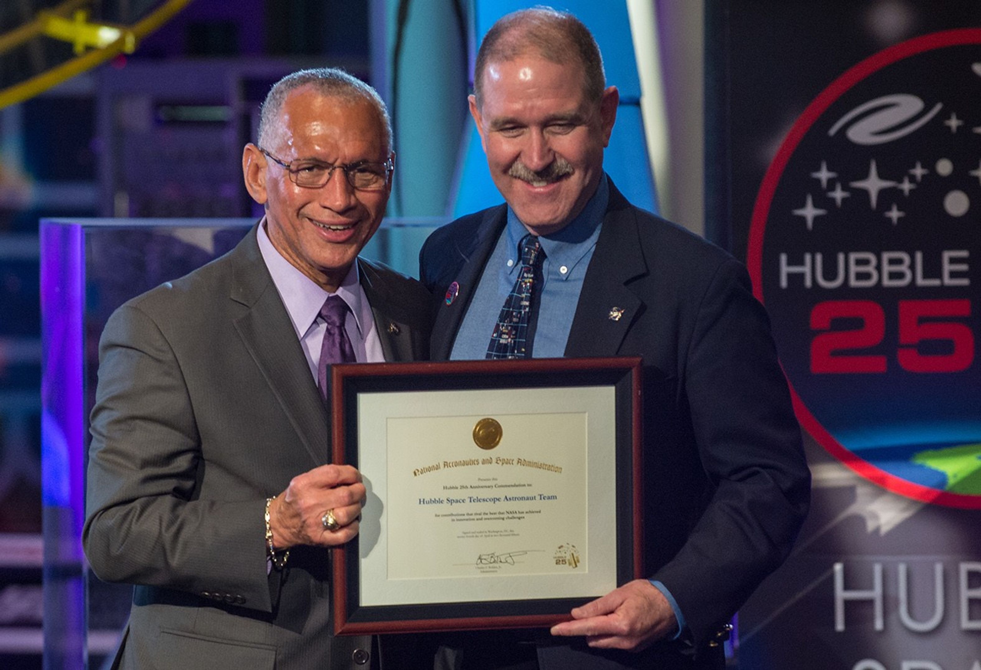 Charlie Bolden and John Grunsfeld stand side-by-side, both holding Grunsfeld's award with one hand each.