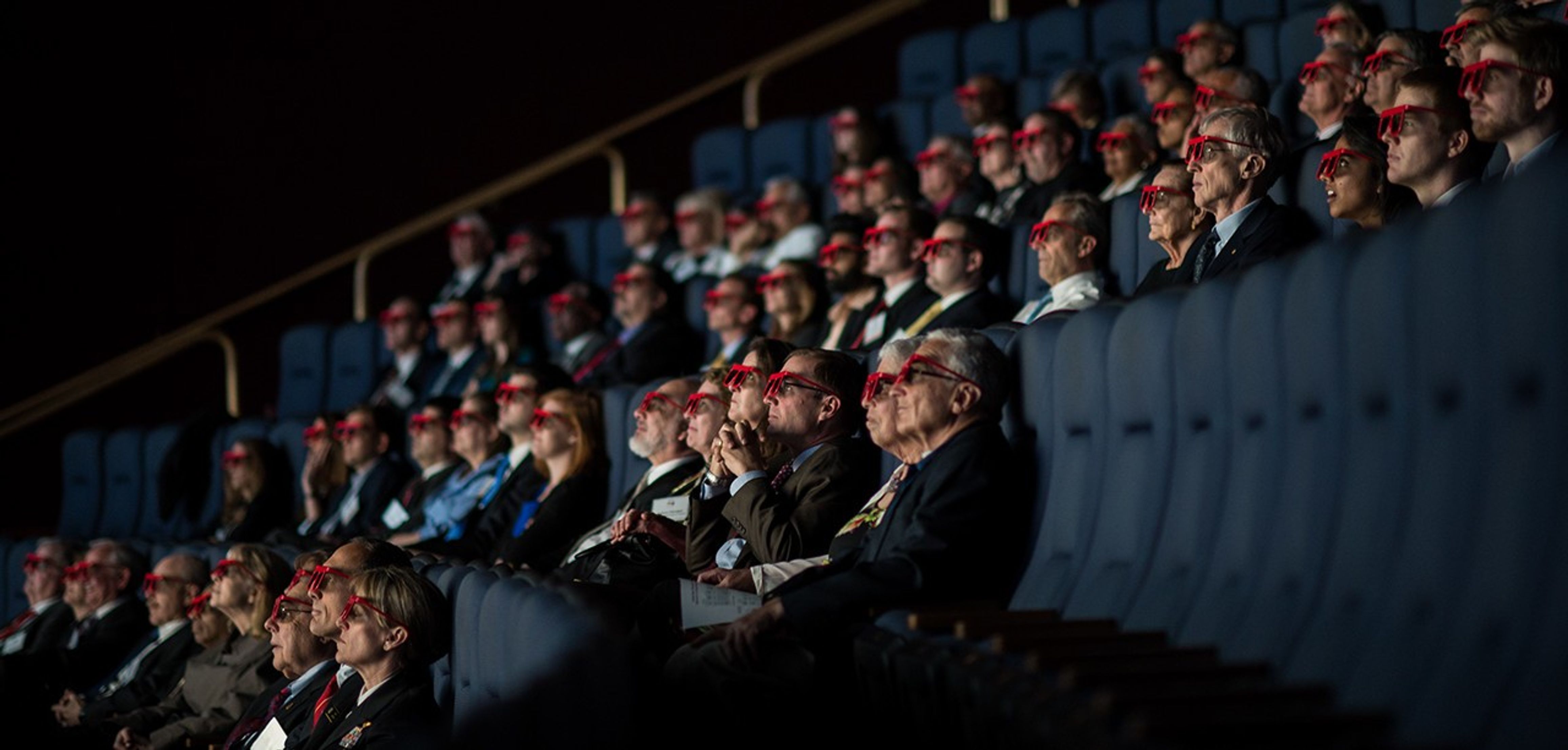 Audience members sit in the seats of the Air and Space Museum's IMAX theater, wearing red 3D glasses.
