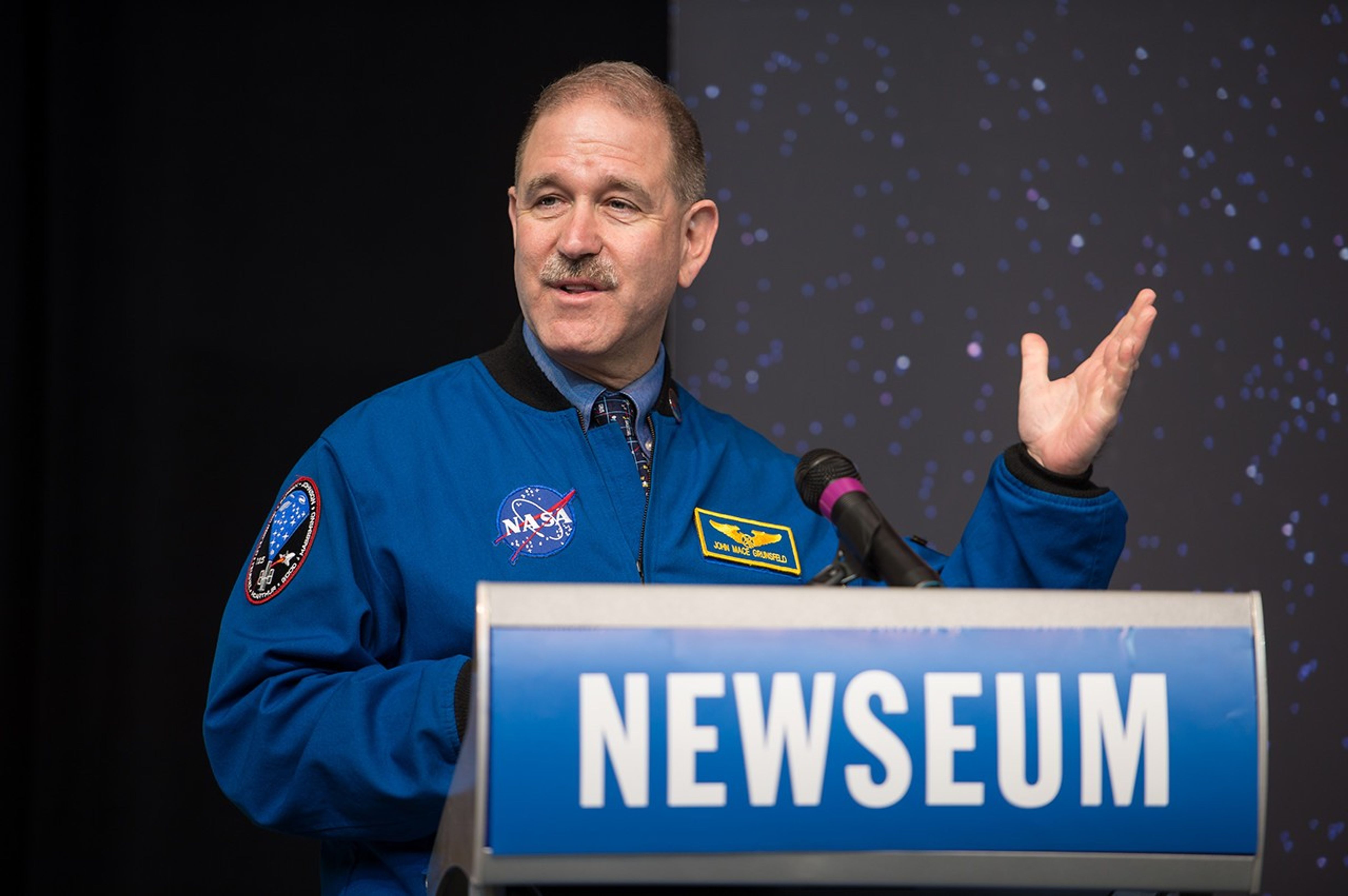 John Grunsfeld stands at the Newseum podium, addressing the audience