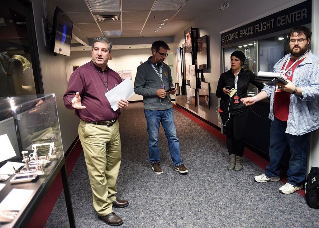 Steve Arslanian (left) explains the astronaut tools in the glass case on the far left to three listening visitors (right).