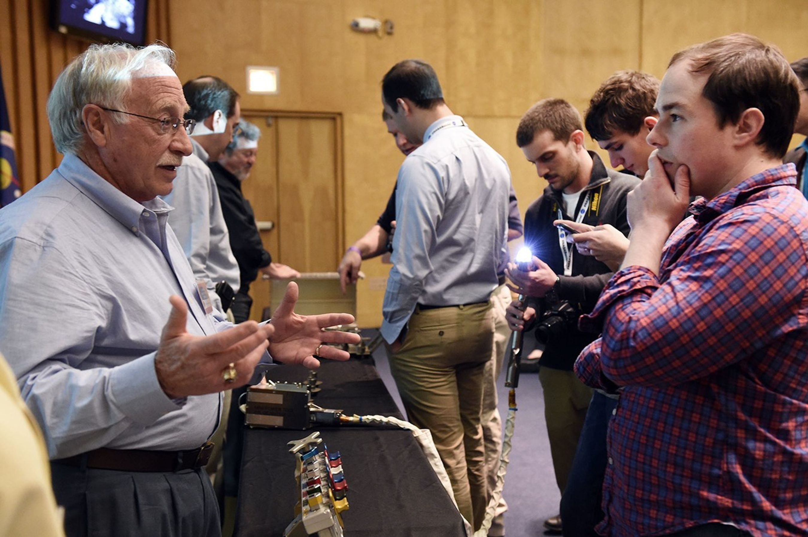 Russ Werneth (left) speaks from behind a table to a male visitor (right), with two more staff members and several more visitors visible in the background.