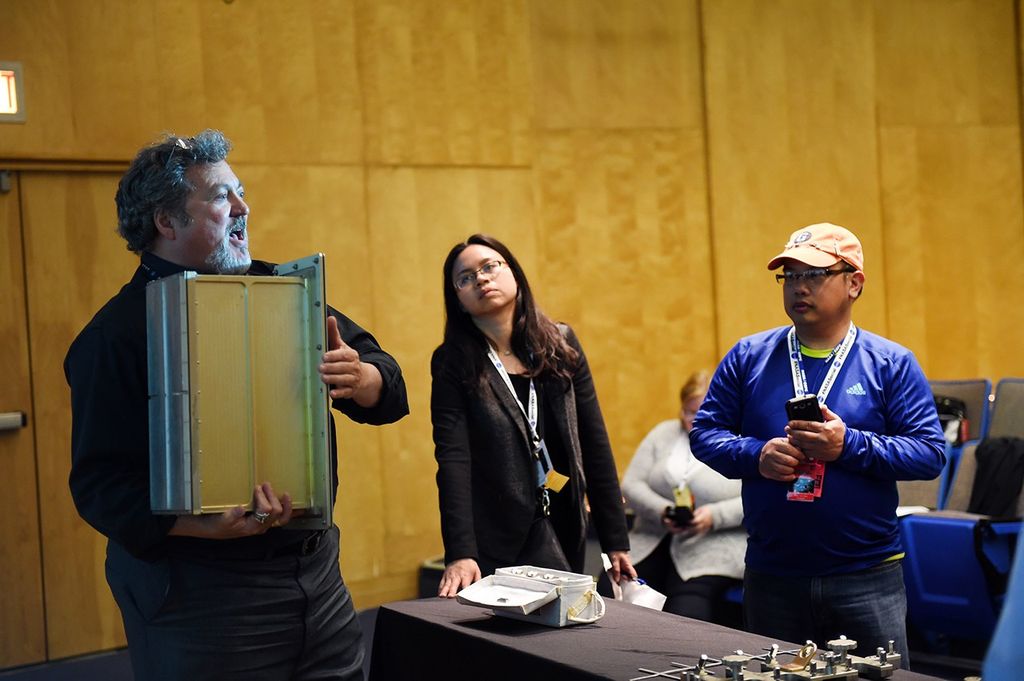Ed Rezac (left) holds a circuit board module while speaking to two listening visitors (right).