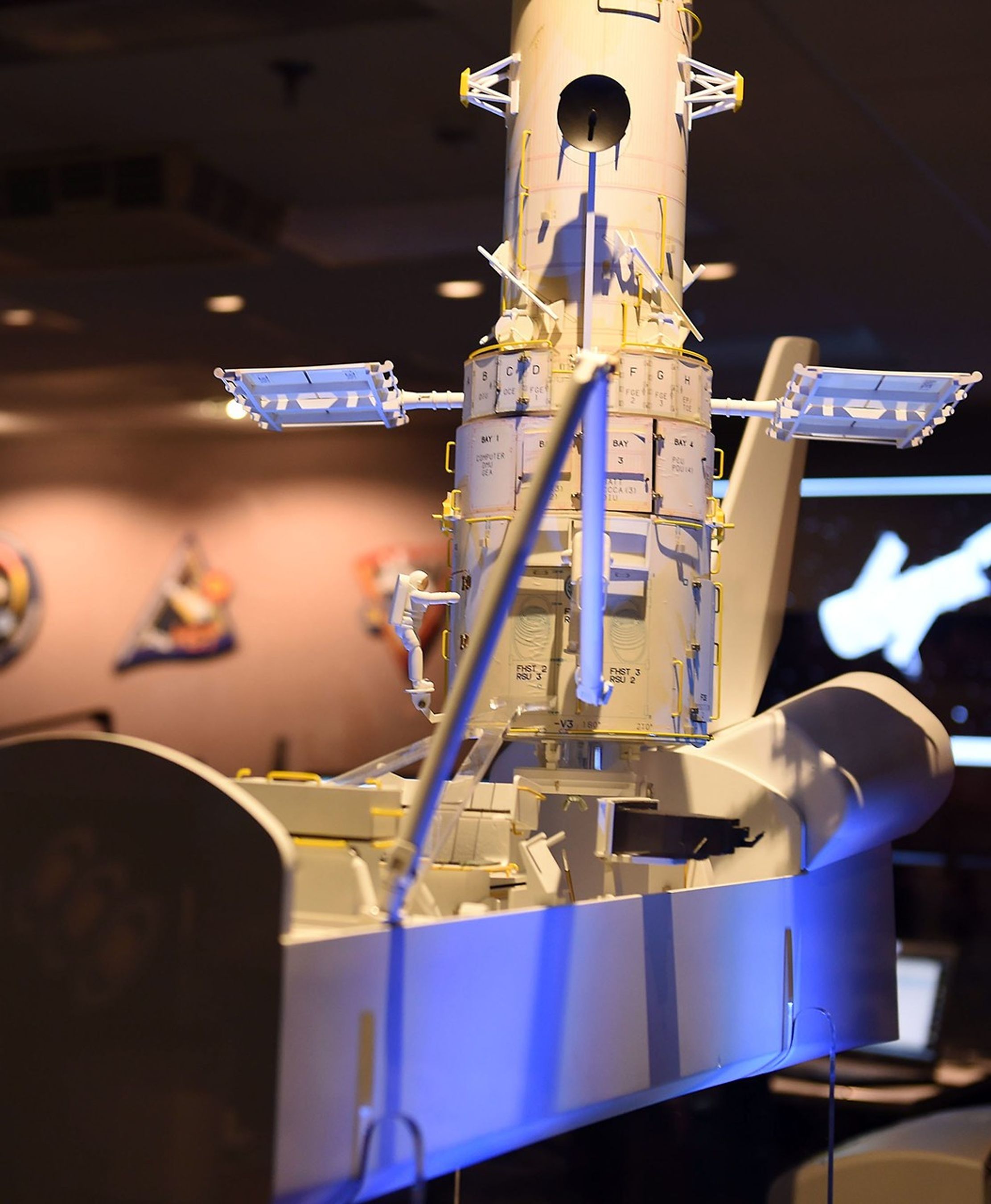 A model of the Hubble Space Telescope sits in the docking bay of a model of a space shuttle. The Operations Support Room is visible in the background.