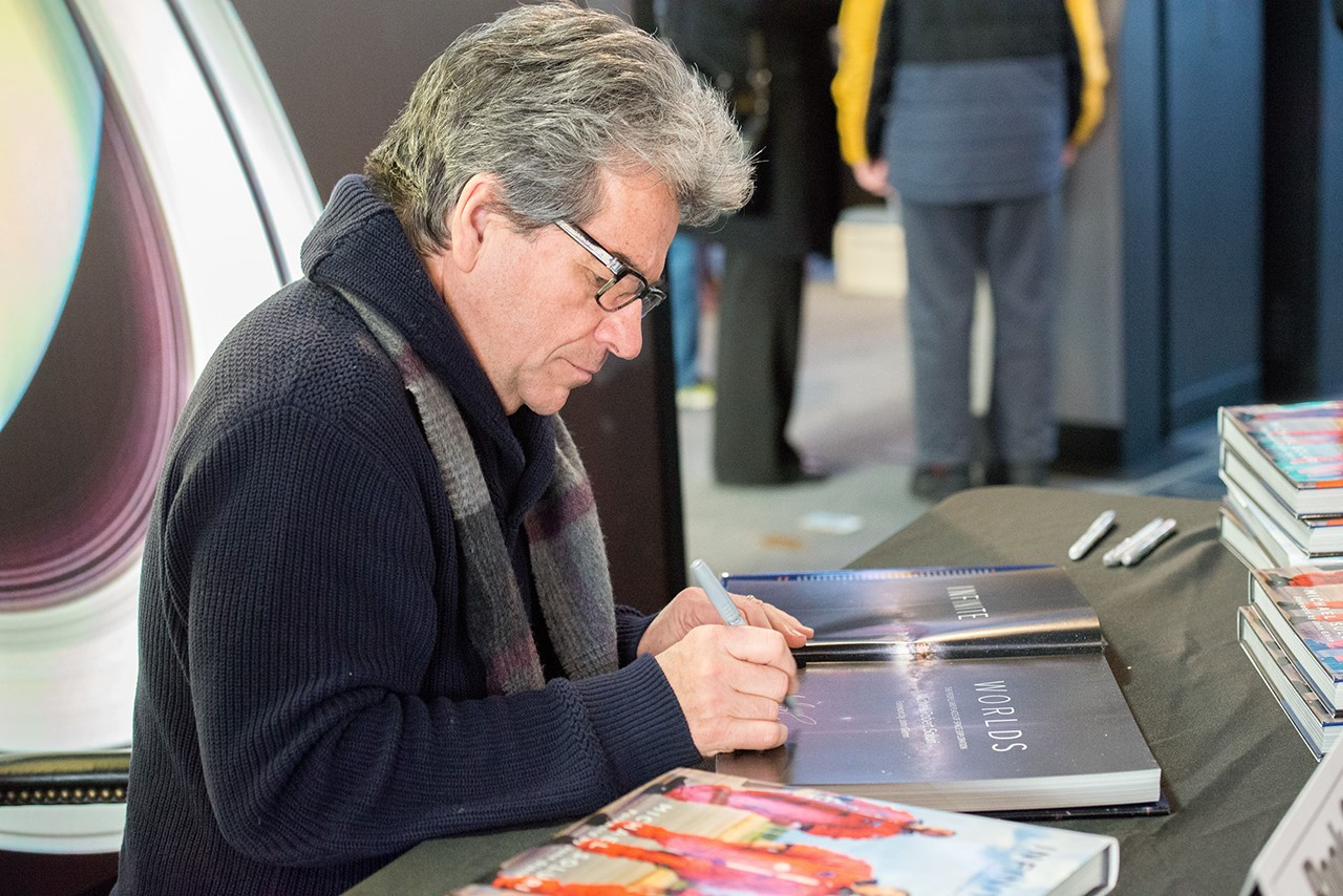 Michael Soluri signs a copy of his book, while several other copies sit on the table nearby.