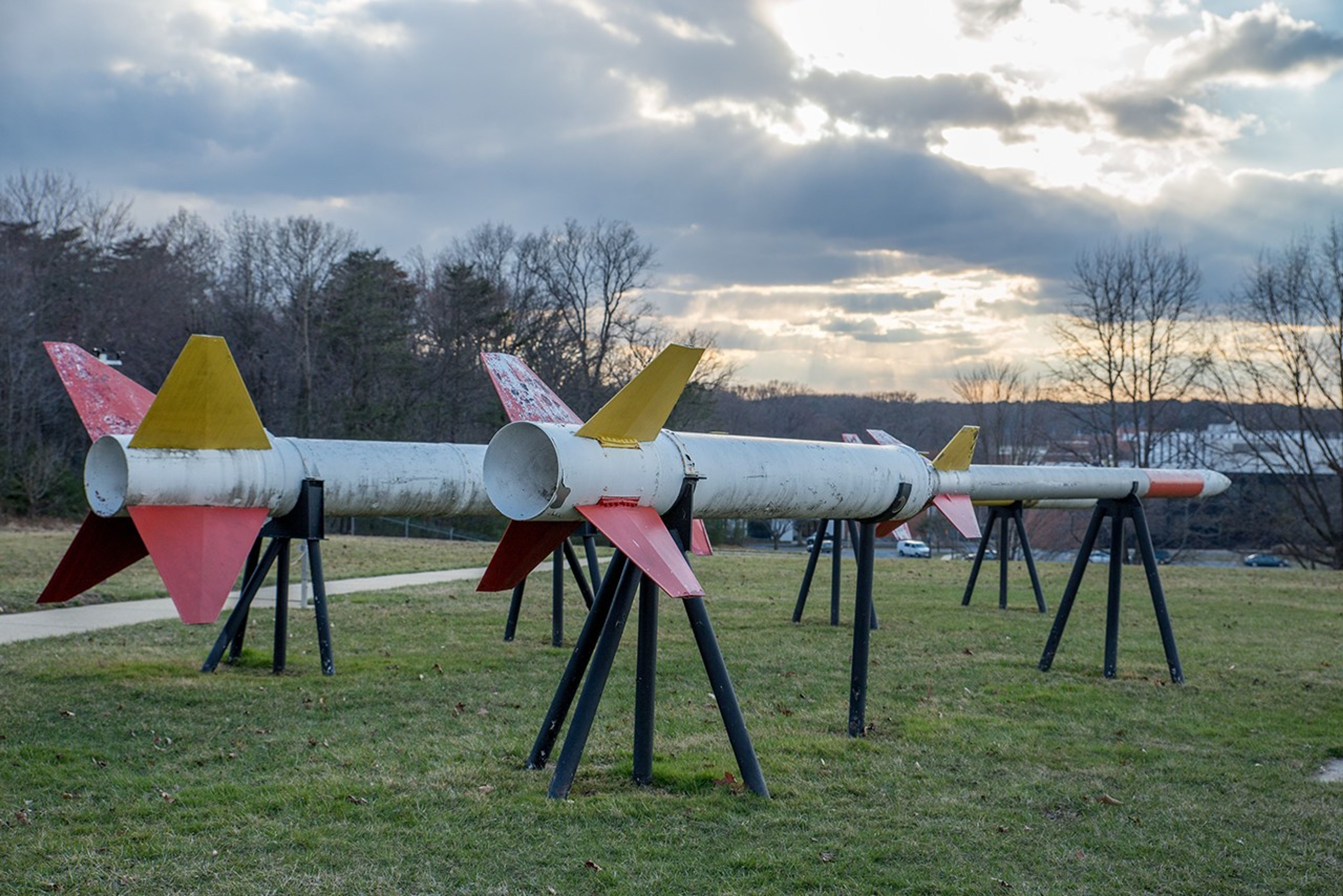 Three sounding rocket models popped up in a grassy field, with a fourth one out of sight behind another, at dusk with partly-cloudy skies.