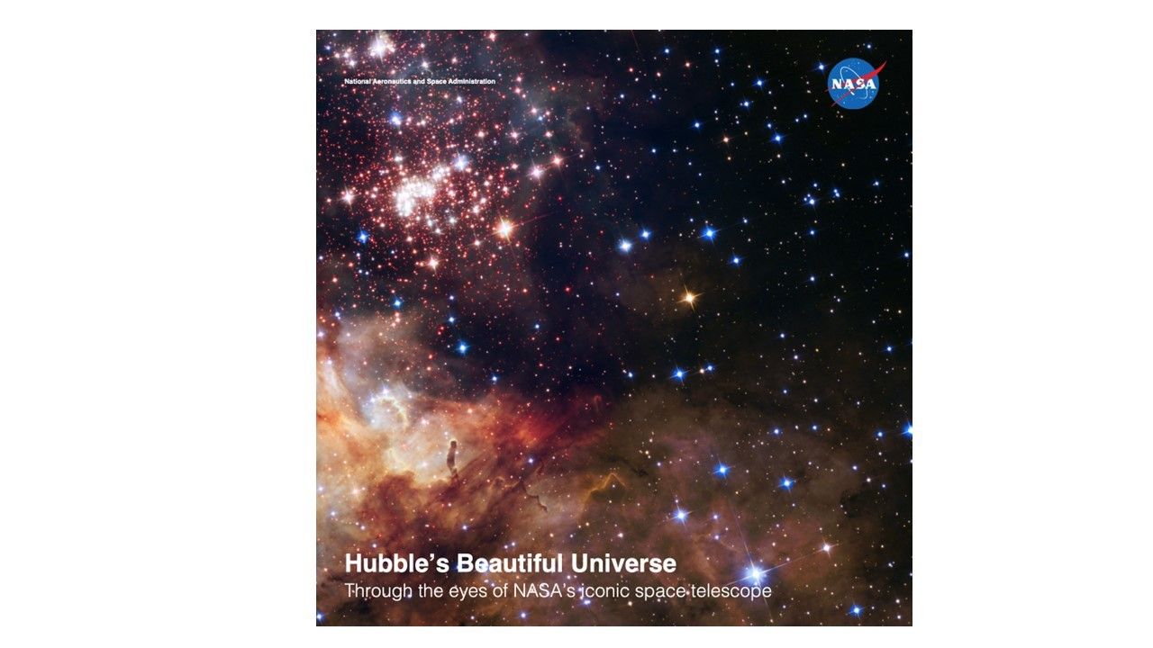 A star cluster fills the upper-left corner of the image. The lower half of the image is filled with billowing clouds of dust and glowing gas. The scene is dotted with white, blue and a smattering of red and yellow stars. All on a black background.