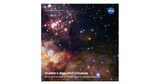 A star cluster fills the upper-left corner of the image. The lower half of the image is filled with billowing clouds of dust and glowing gas. The scene is dotted with white, blue and a smattering of red and yellow stars. All on a black background.