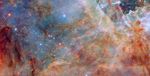 A section of Tarantula Nebula that holds layers of colored clouds of gas with varying thickness. In the background are bluish, translucent, and wispy clouds; on top of these are stretches of redder and darker, clumpy dust, mostly along the bottom and right. In the bottom left corner are some dense bars of dust that block light and appear black. Small stars are scattered across the nebula.