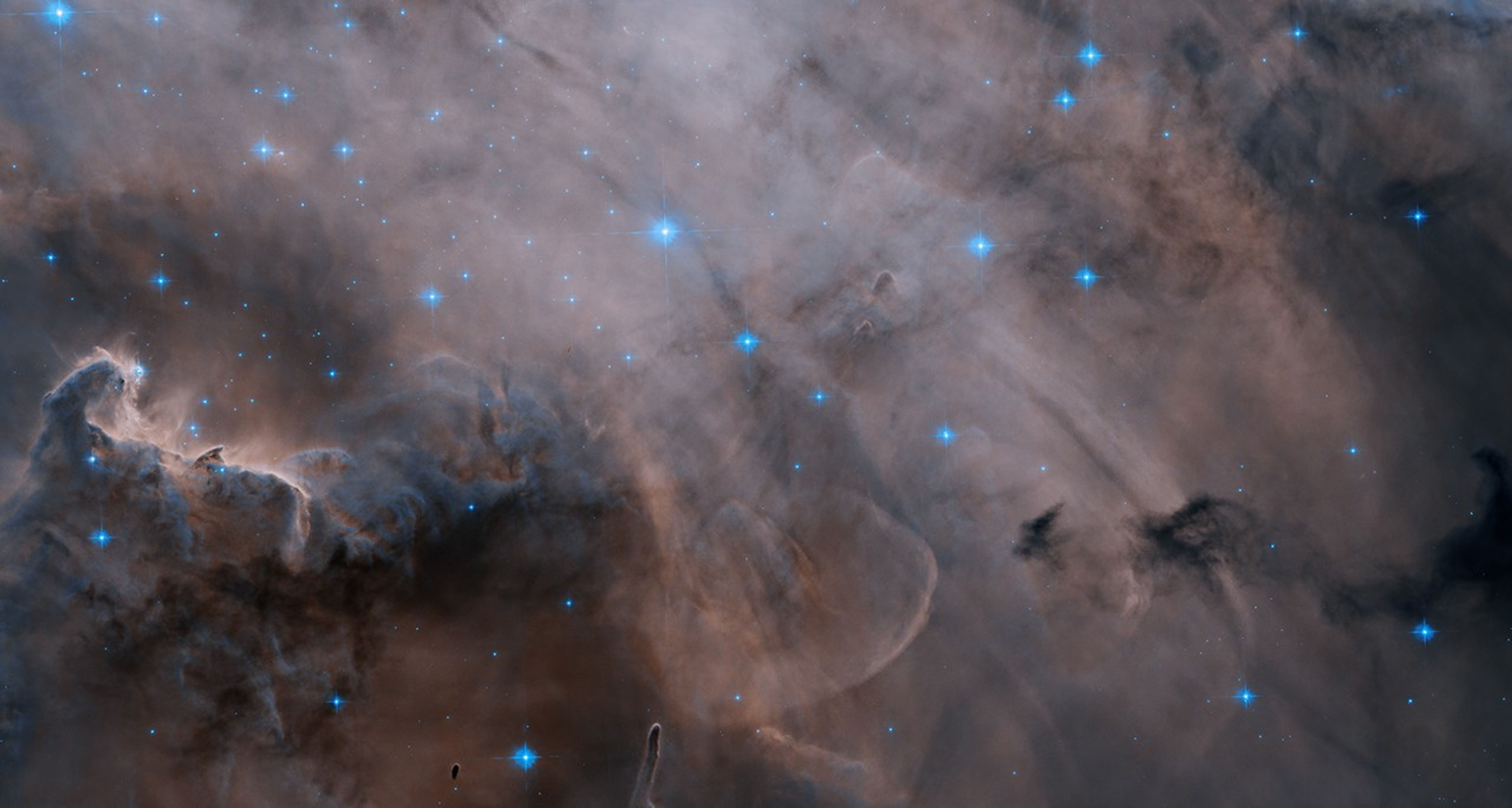 Wisps of pinkish-grey clouds fill the scene. Patches of dark dust obscure the glow. Bright, blue-white stars shine through the cloud.  The words "New Image" in a red box on the upper-right side of the image.