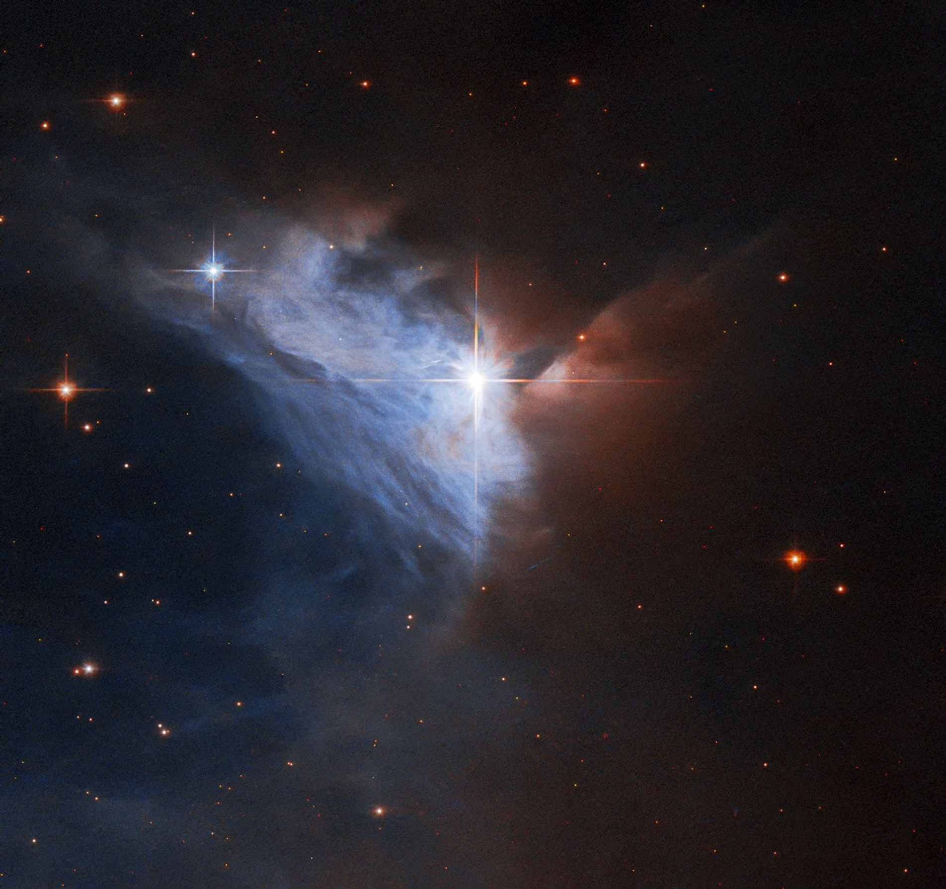Near the center of the image shines a bright star with four spikes. It forms a vertex of a triangle of wispy blue and blue-white light that forms the emission nebula taking up about a third of the image. To the right and above the bright star, the image quickly fades from pale red to black, which is where a dense cloud of dust blocks our view of the nebula.