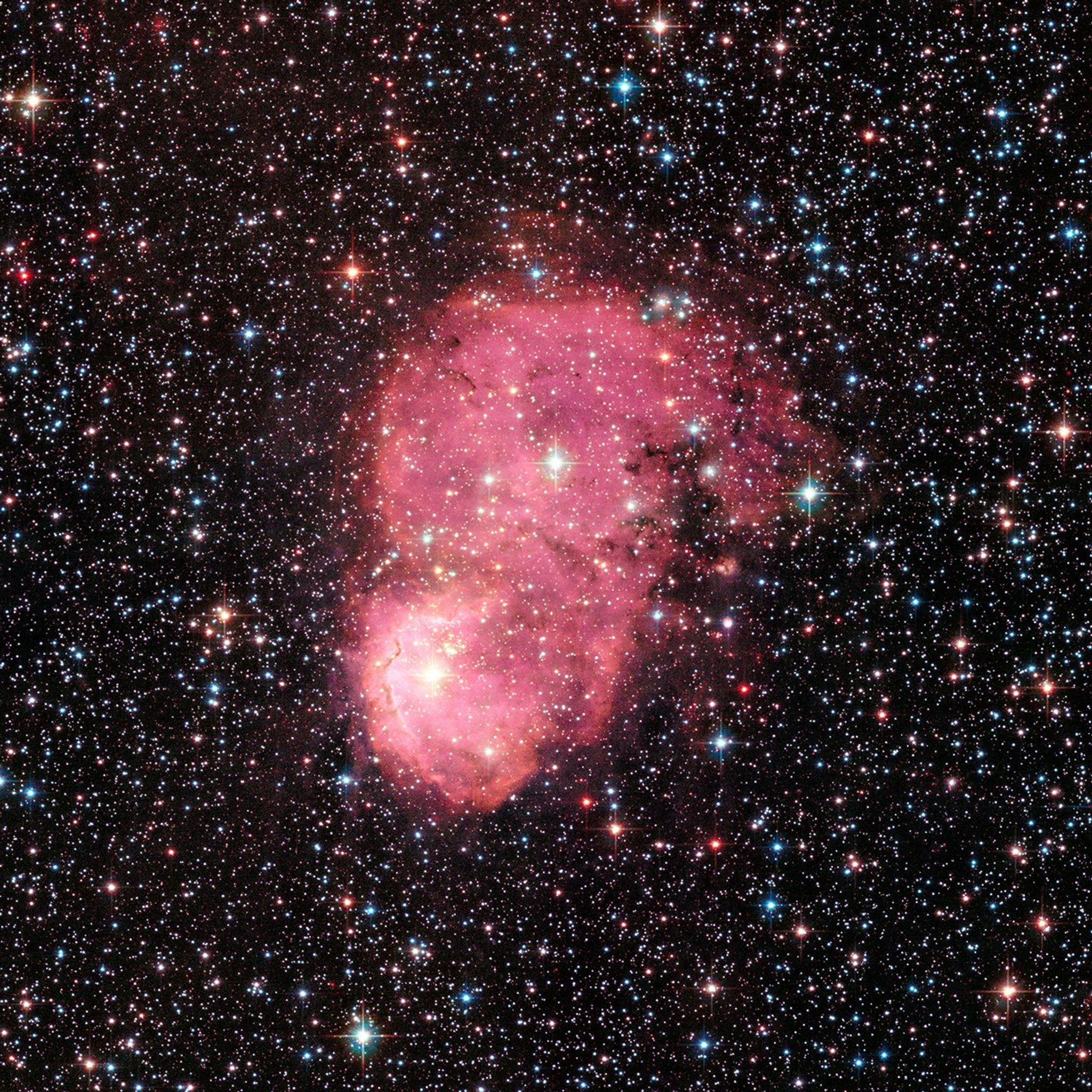 The center of the image displays a combination of two nebulas, red clouds of gas and dust, that are close to each other. On the left and right is a massive number of stars and galaxies, which appear as red, green, and blue dots. The brightest stars have plus-sign-shaped diffraction spikes.