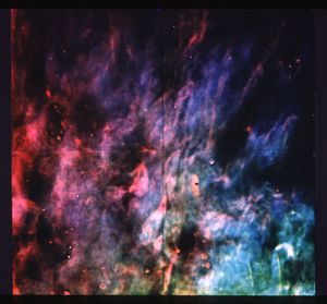 A nebula that strongly resembles flames in terms of shape. On the left side of the image, they're colored more red and pink, then blend into purple near the center, and then to light blue and dark green on the right.