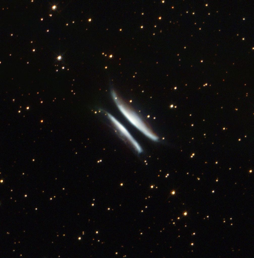 Two white, hyperbolic/bow-shaped arcs of gas and dust with what appears to be a black streak passing through the middle, set against a black backdrop with hundreds of stars.