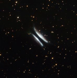 Two white, hyperbolic/bow-shaped arcs of gas and dust with what appears to be a black streak passing through the middle, set against a black backdrop with hundreds of stars.