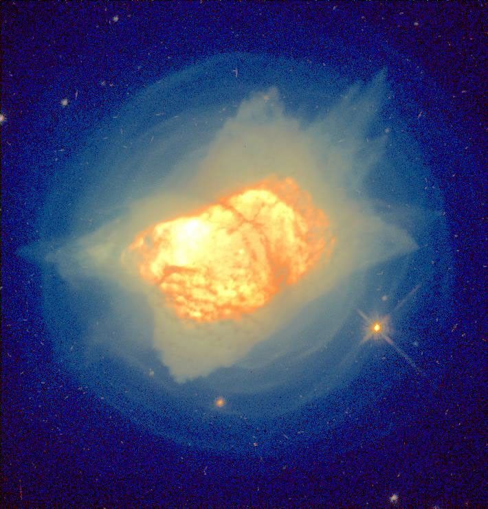 Bright yellow-orange cloud of dust and gas forming a glob in the center with thin light-yellow gas surrounding it, while the outer edges are blue.