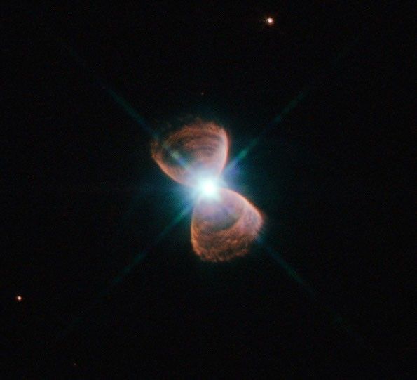 Two hourglass-shaped red lobes of gas, with a bright star at the center, against a black background.