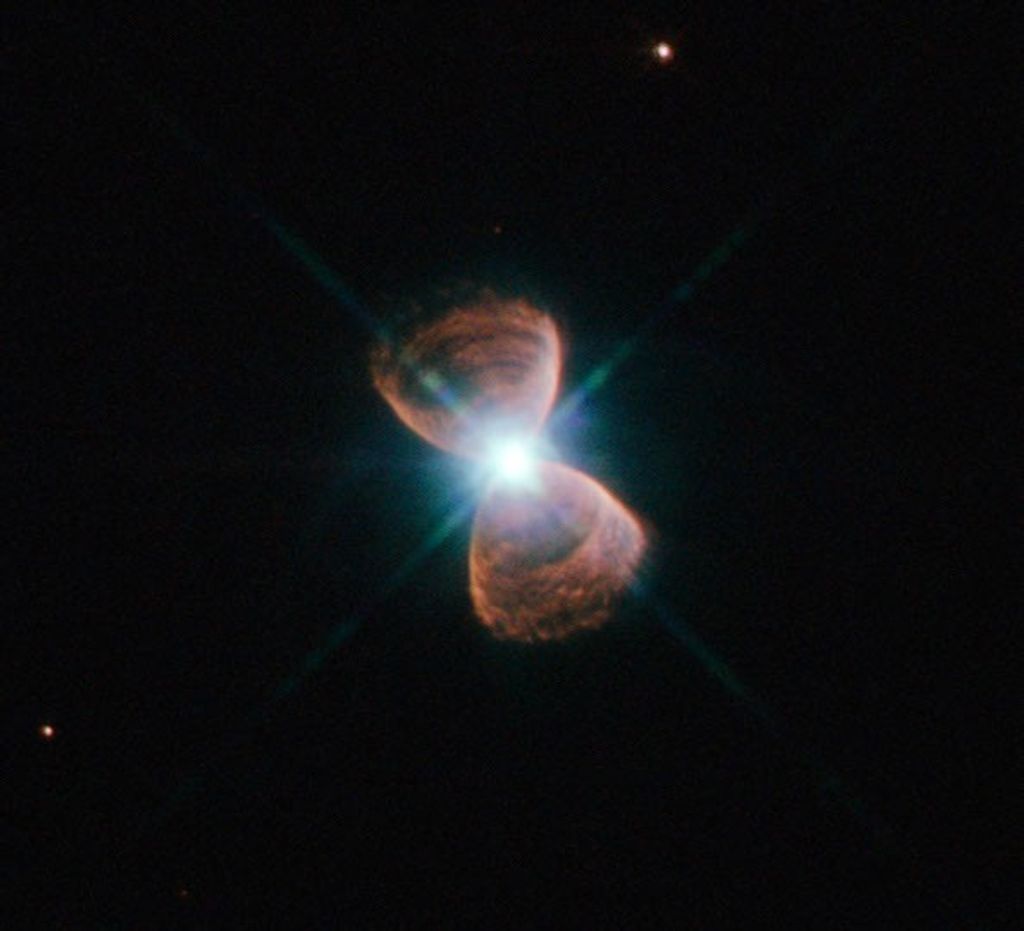 Two hourglass-shaped red lobes of gas, with a bright star at the center, against a black background.