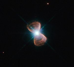 Two hourglass-shaped red lobes of gas, with a bright star at the center, against a black background.